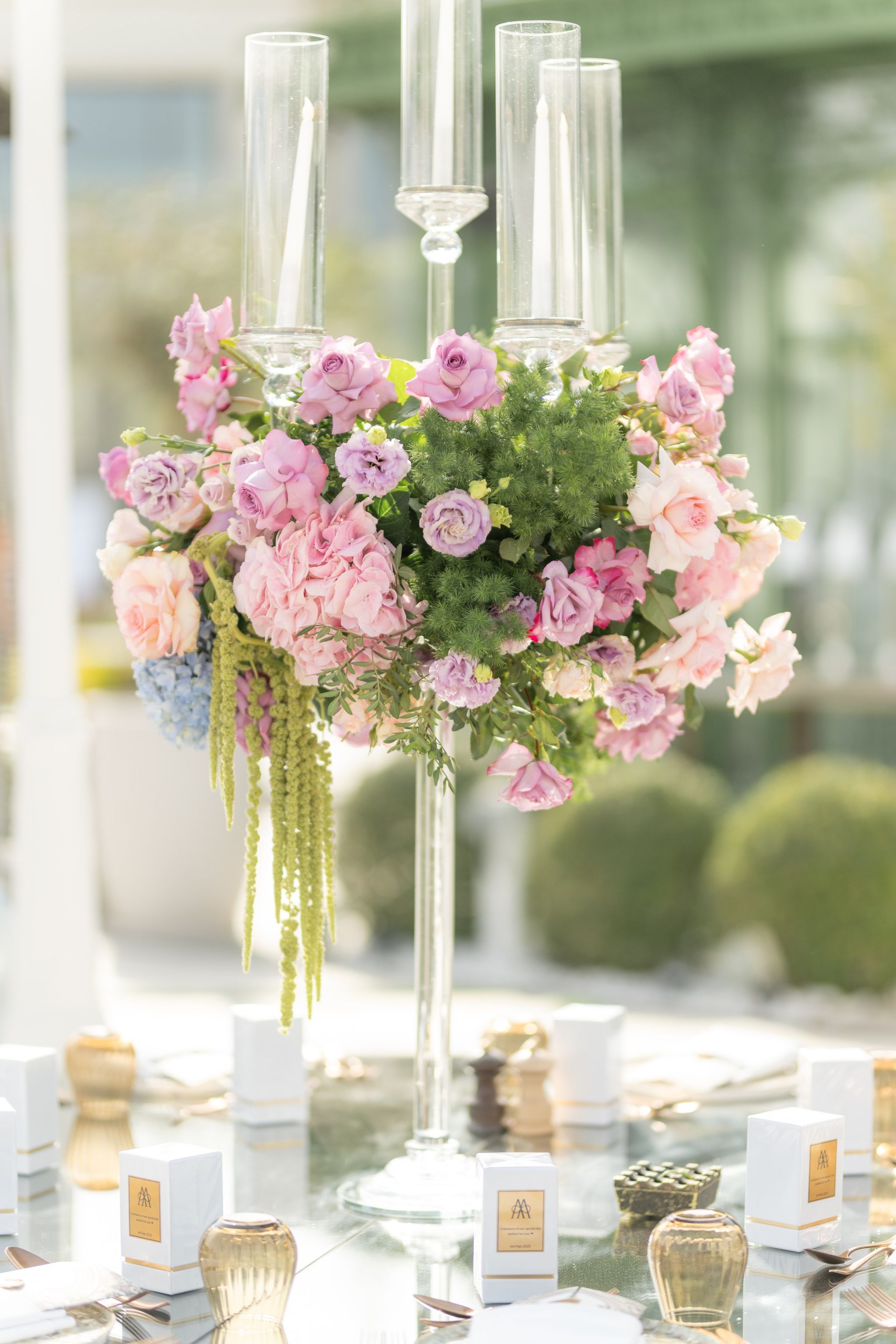 Close view of a candelabrum arrangement of roses, hydrangea and trailing amaranthus over a set table