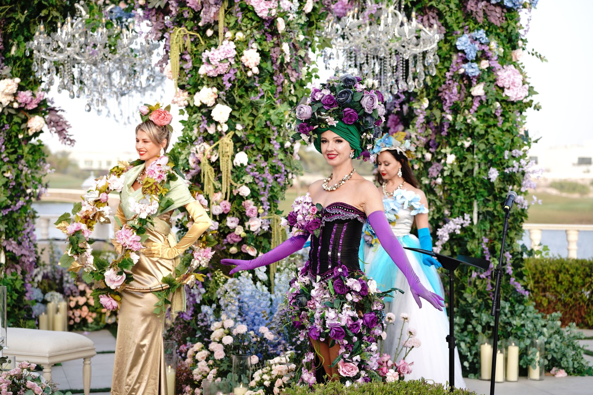 Performers in floral corsets, gowns and headdresses before the wisteria canopy