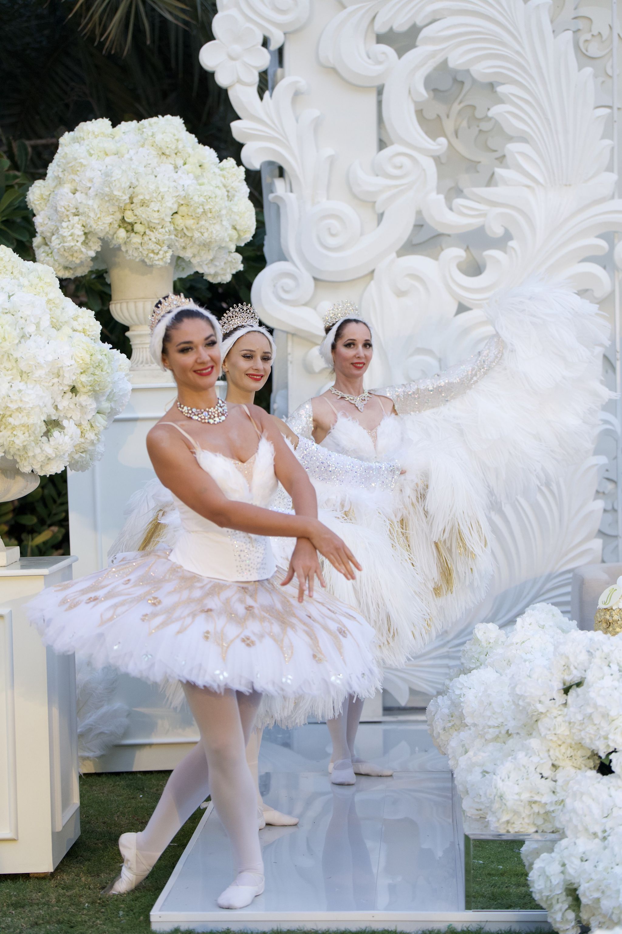 Three ballerinas in white and gold tutus beside urns of hydrangeas at Raffles The Palm Dubai