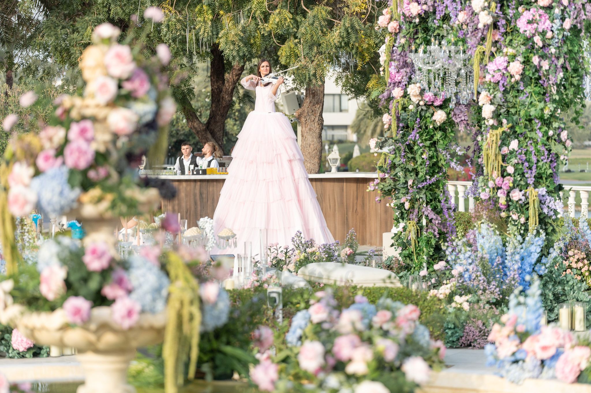 Violinist in a tiered blush gown playing above the garden, framed by the floral canopy