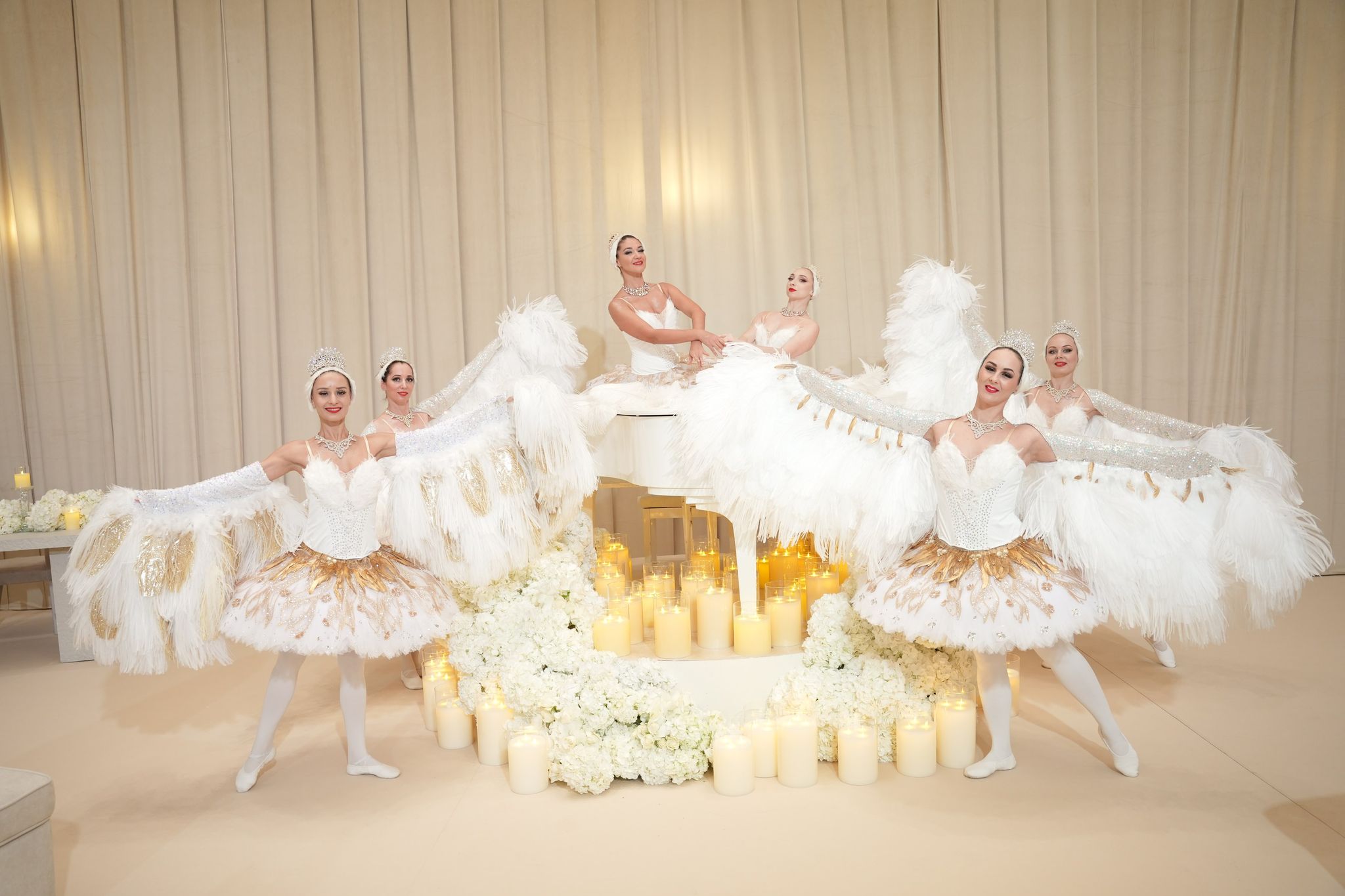 Ballerinas in white and gold tutus fanning feathered wings around a candlelit grand piano at Raffles The Palm Dubai