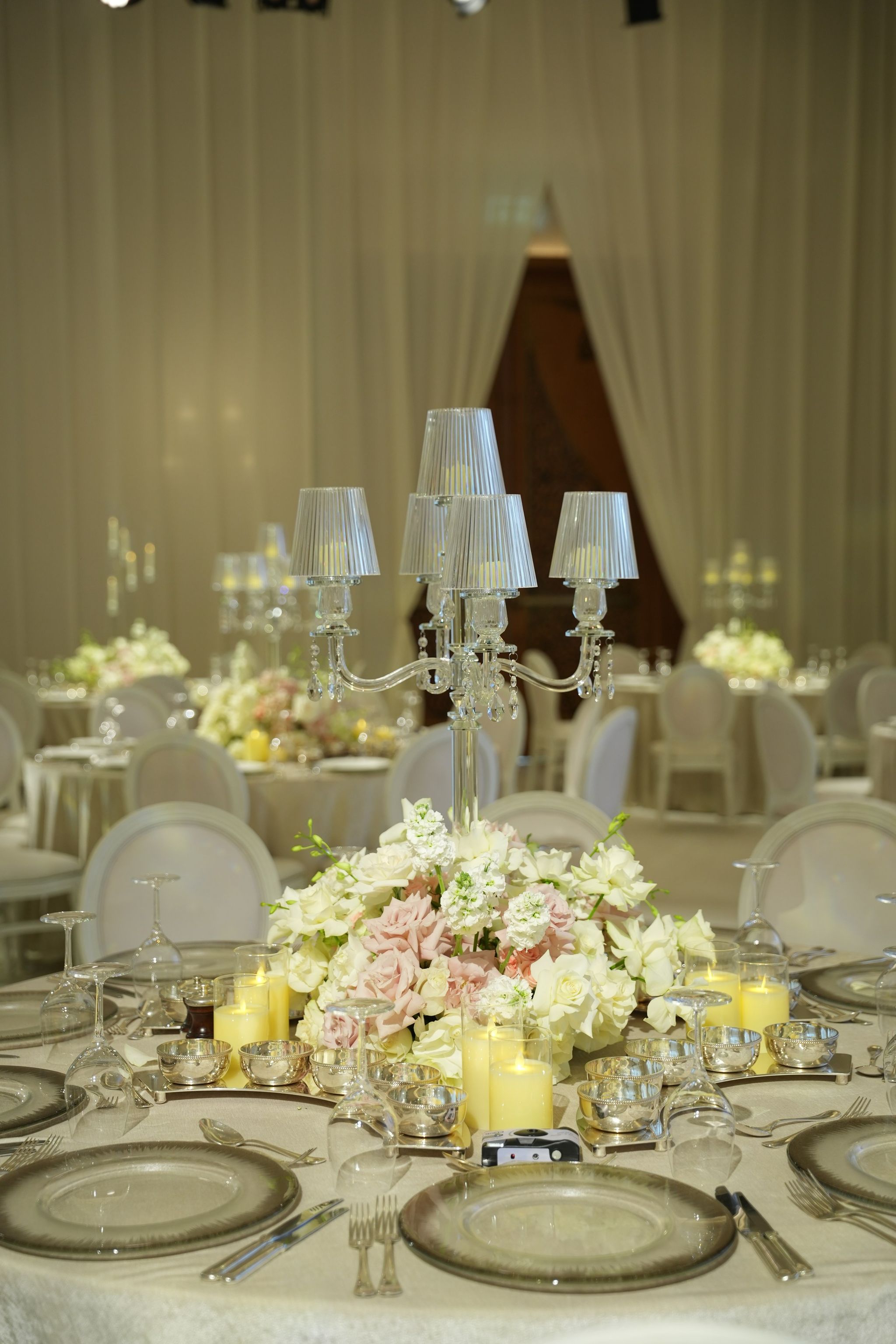 Shaded crystal candelabra over low white and pink roses, silver bowls and smoked chargers