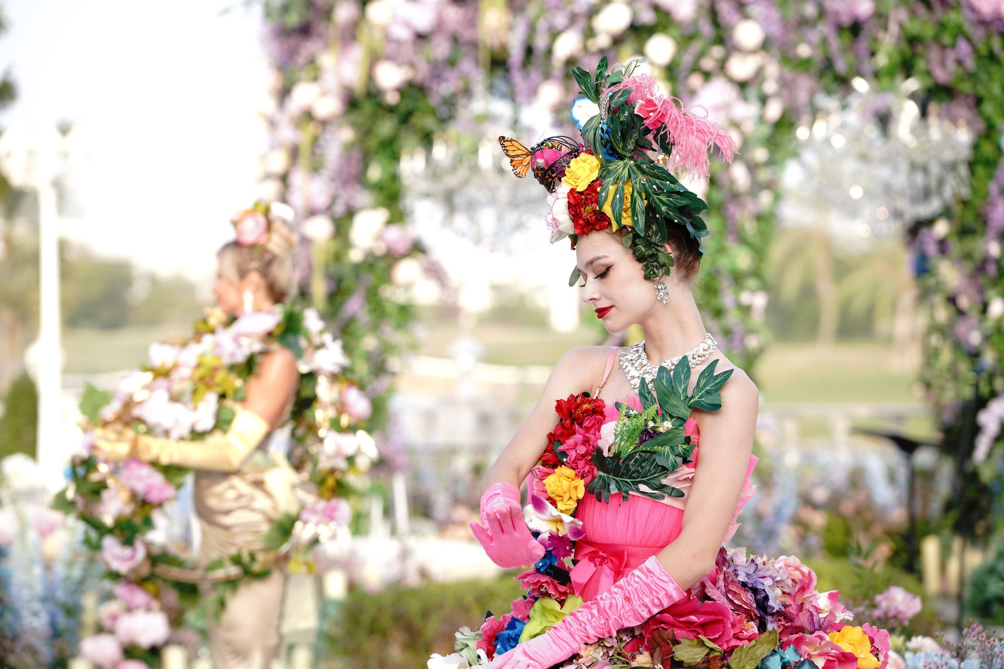 Performer in a rose and butterfly headdress and pink gloves holding a floral skirt