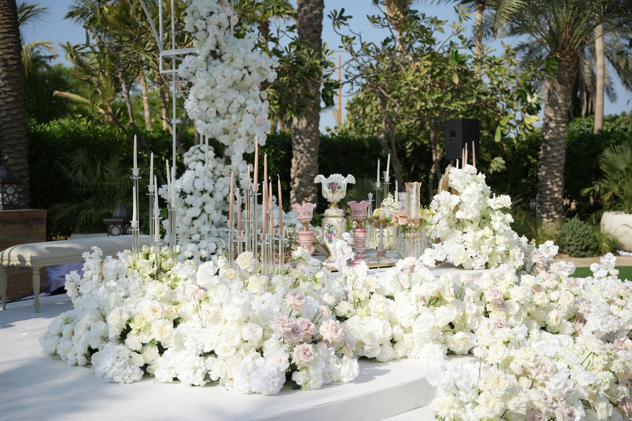 Ceremony stage banked with white roses and hydrangeas, crystal candelabra and pink opaline lamps