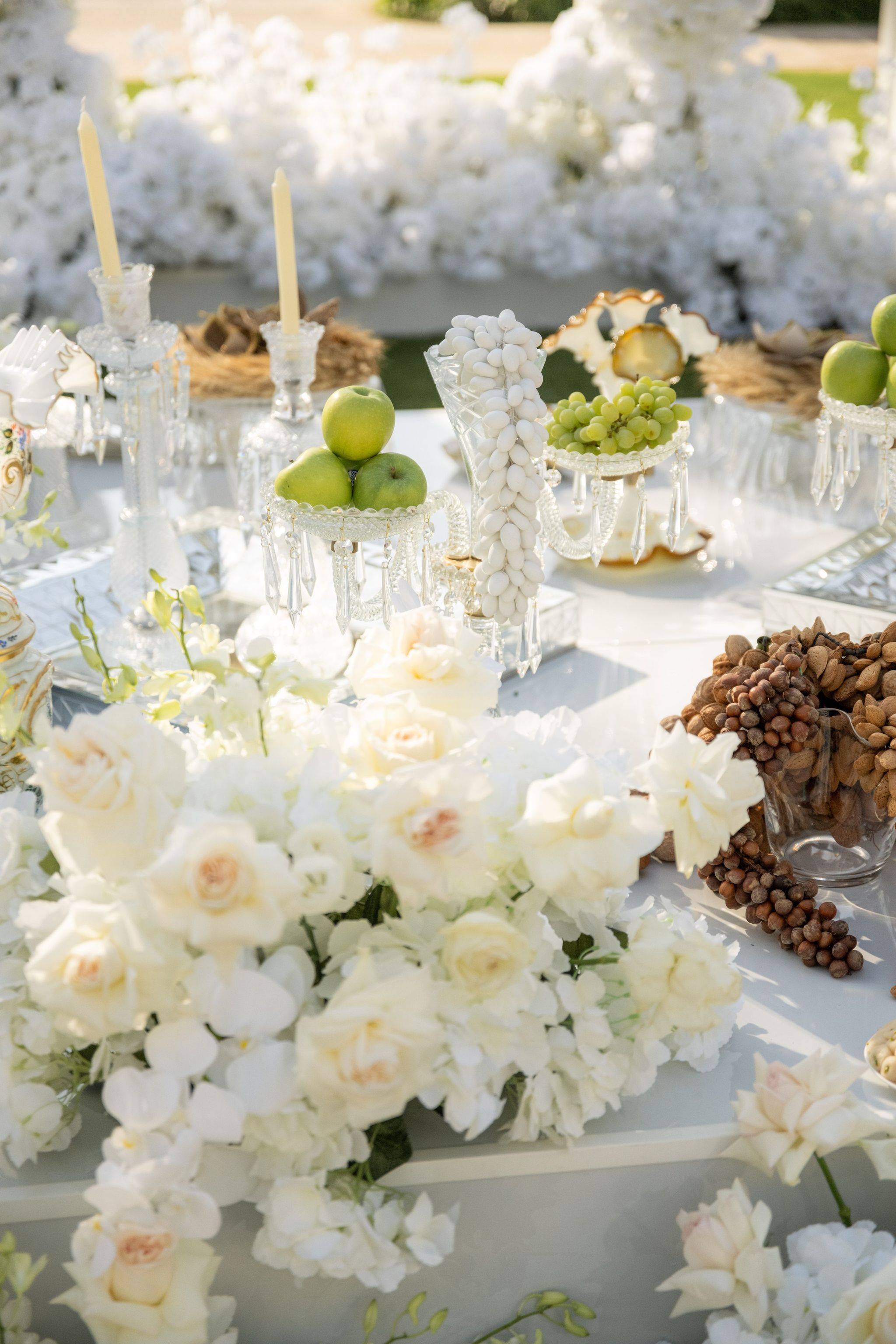 Sofreh detail of sugared almonds, green apples, grapes and pine cones among white roses