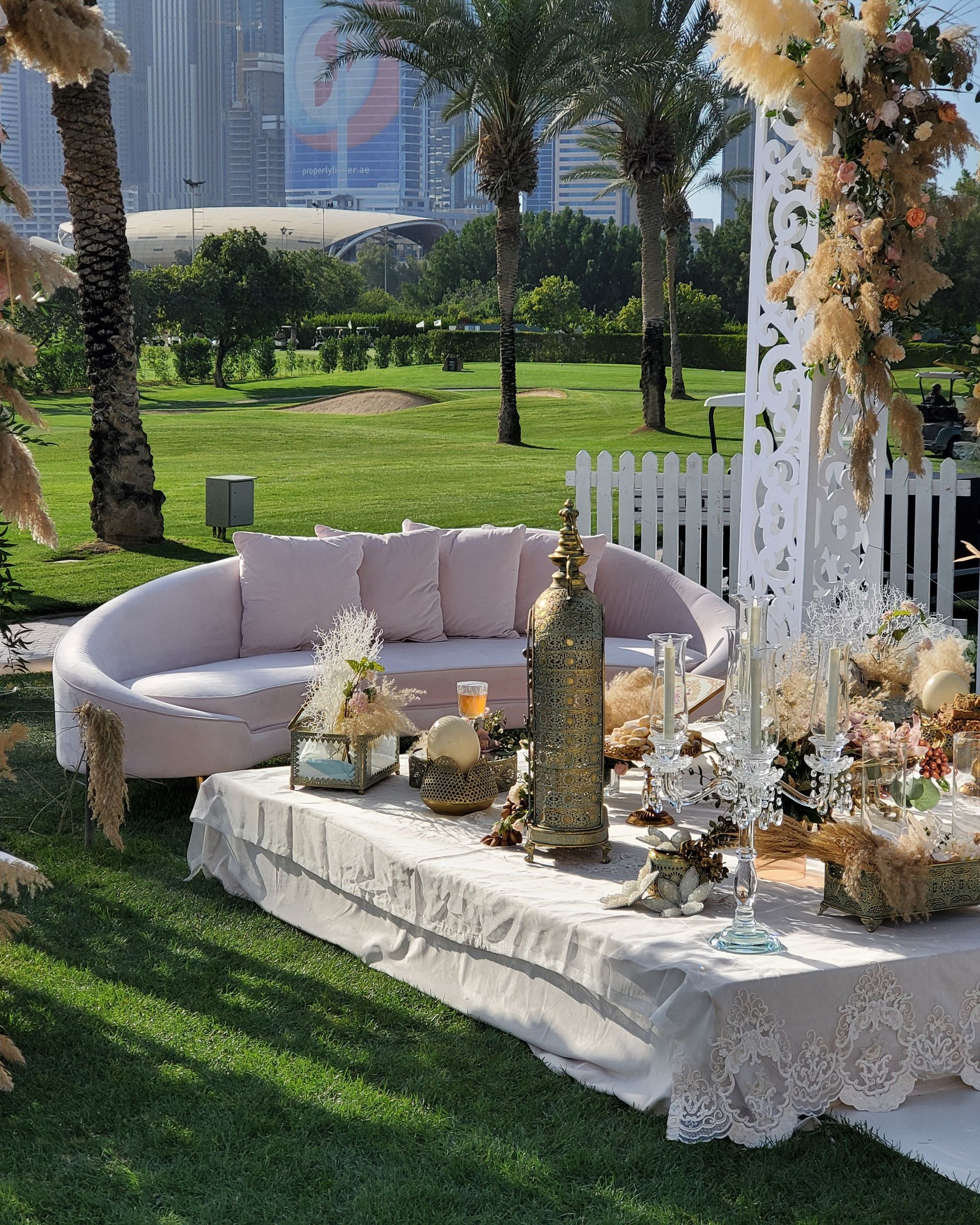 Blush curved sofa and lace-draped ceremony table framed by carved white panels and pampas at Emirates Golf Club