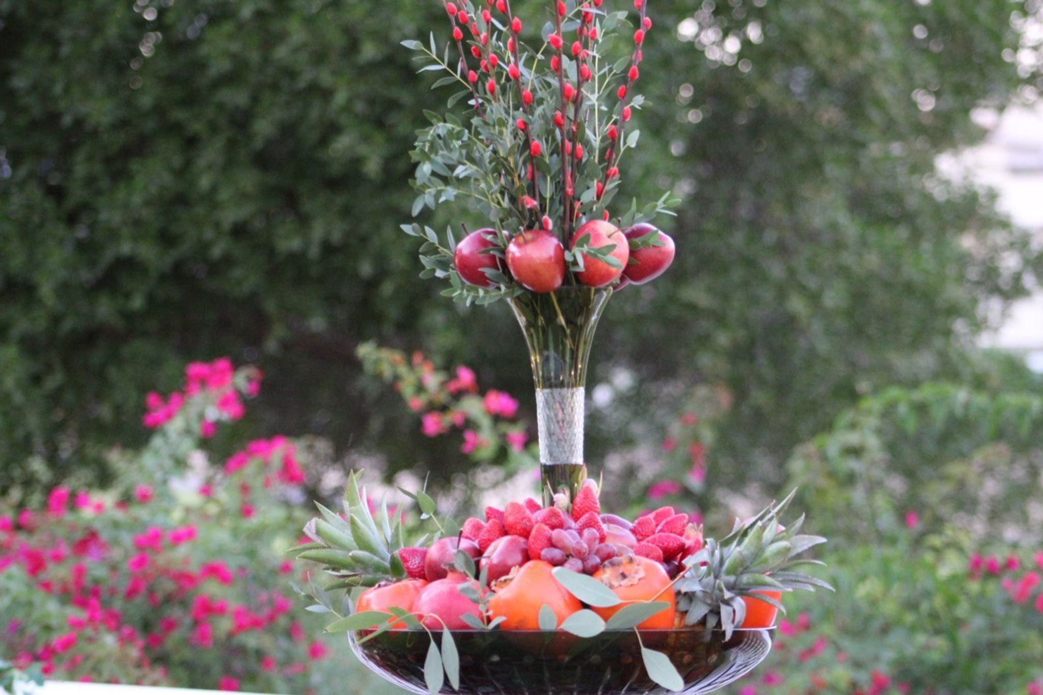 Pomegranates and red berry stems over a bowl of strawberries, persimmons and pineapple