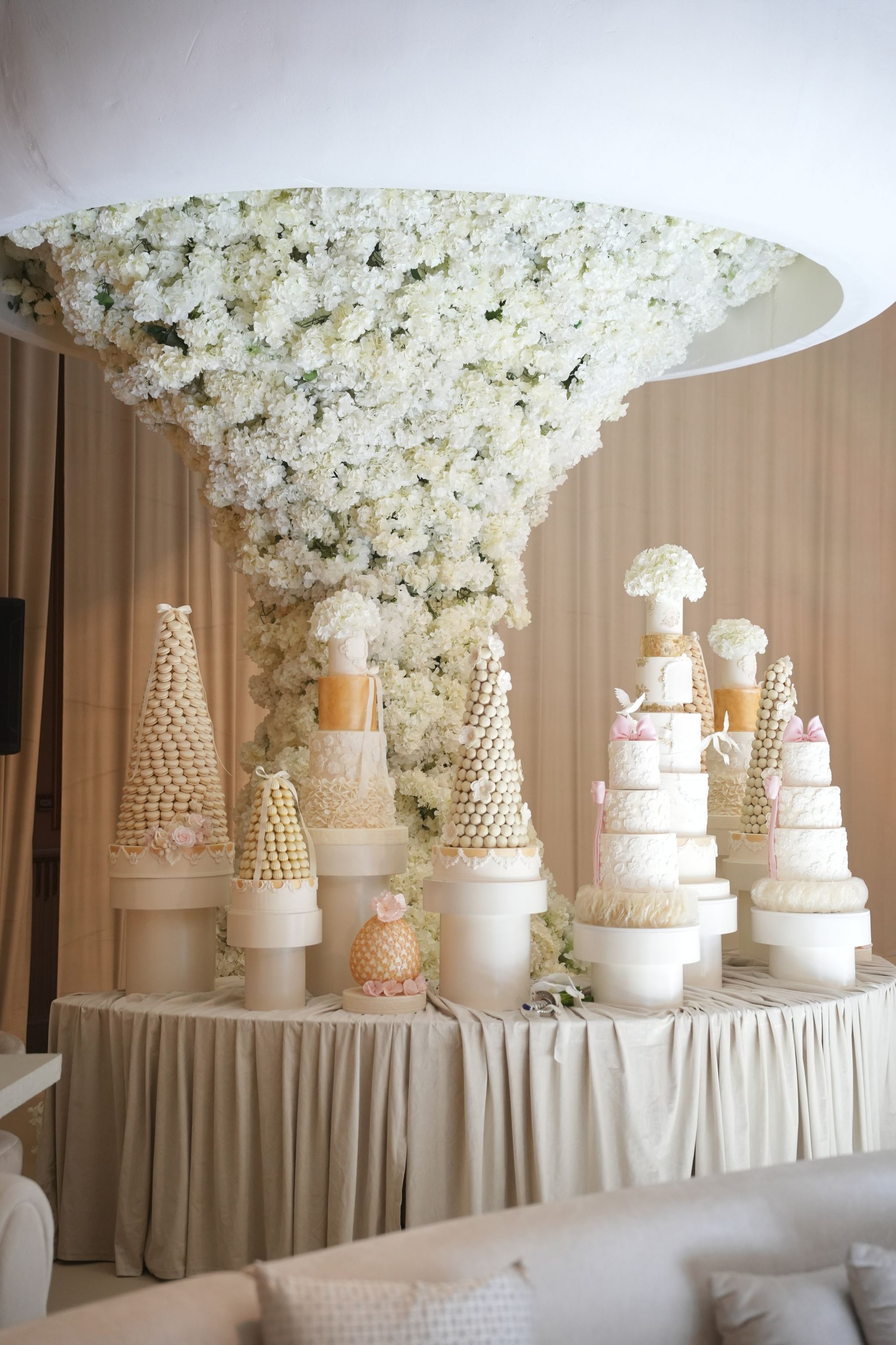 Croquembouches and white tiered cakes beneath a cascade of white hydrangeas falling from a suspended canopy