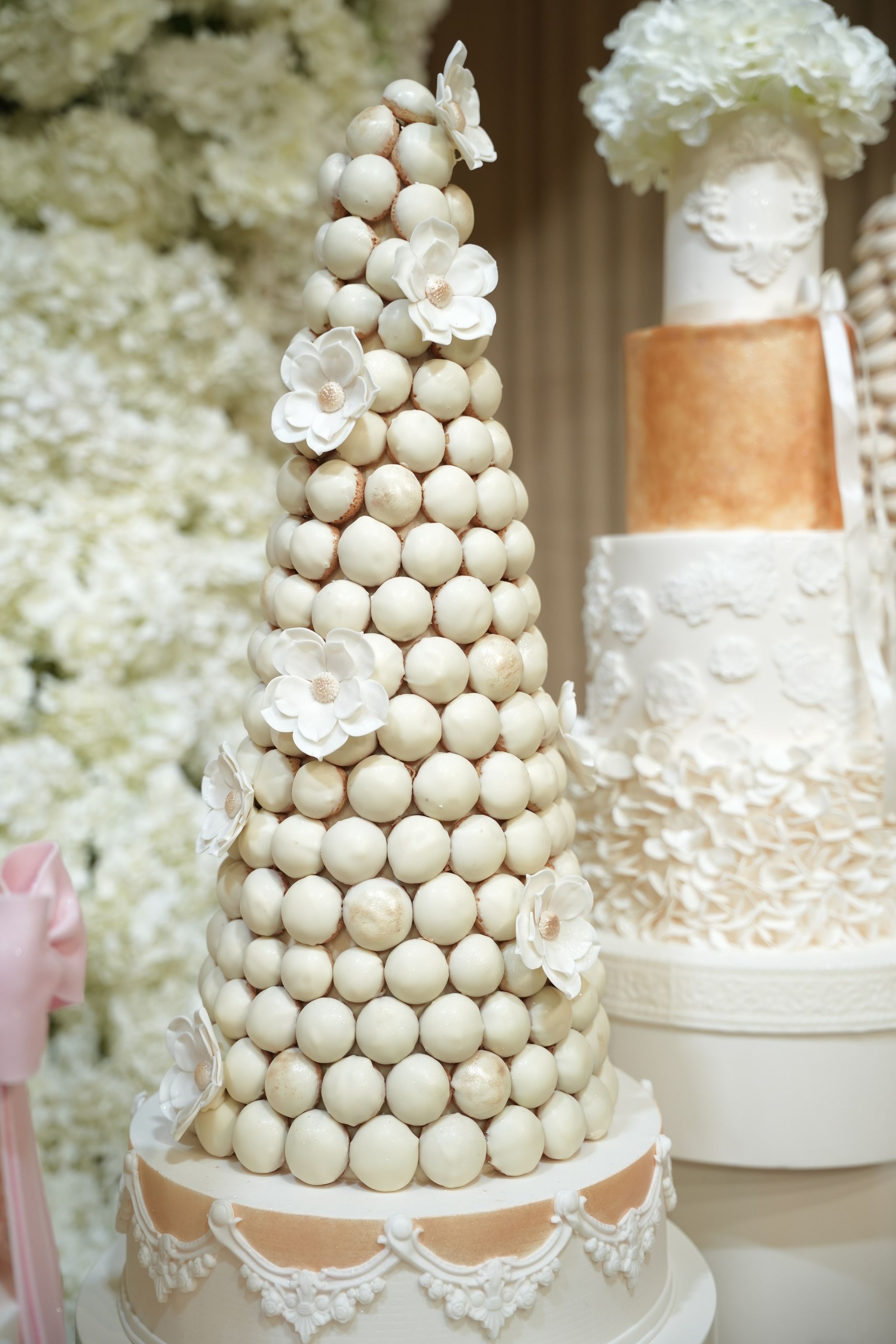Croquembouche decorated with sugar flowers beside a white and copper tiered wedding cake
