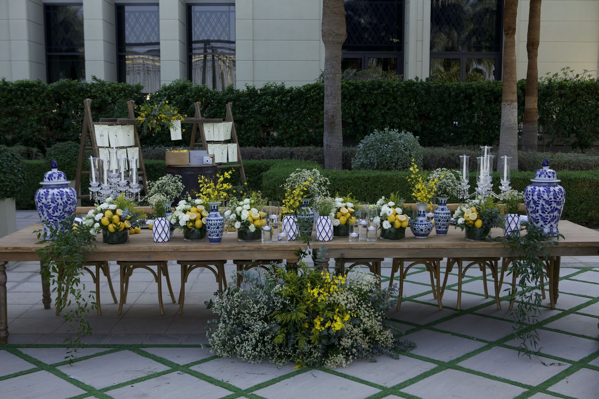 Rustic table of yellow roses, mimosa and blue-and-white ginger jars before the seating plan