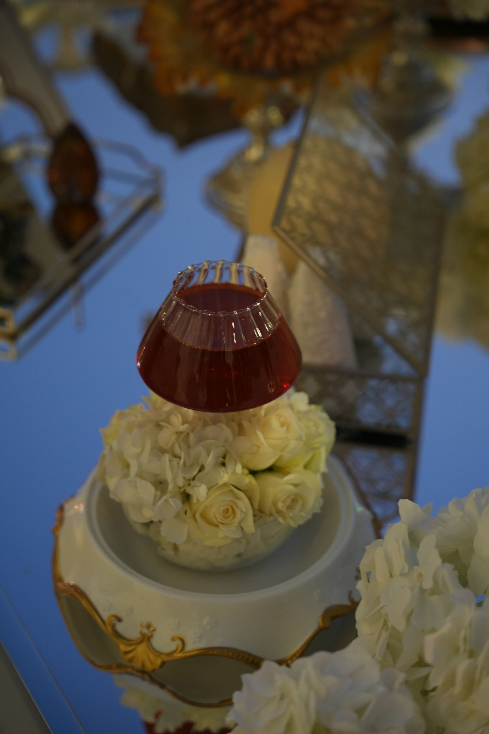 Crimson glass cup set into a ring of ivory roses on a gilded porcelain bowl