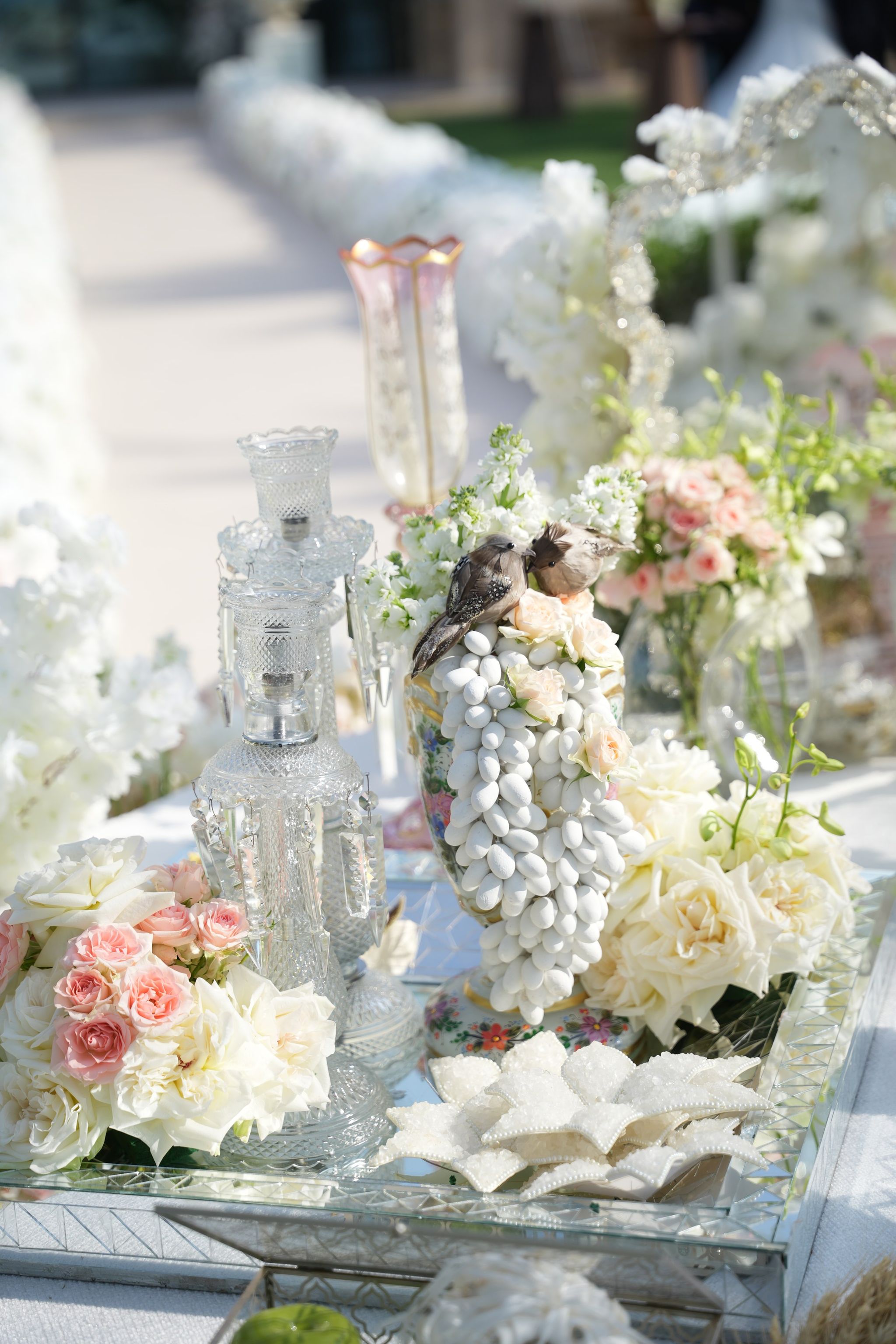 Crystal decanter and sugared-almond sculpture with bird figurines, white floral aisle softly blurred behind
