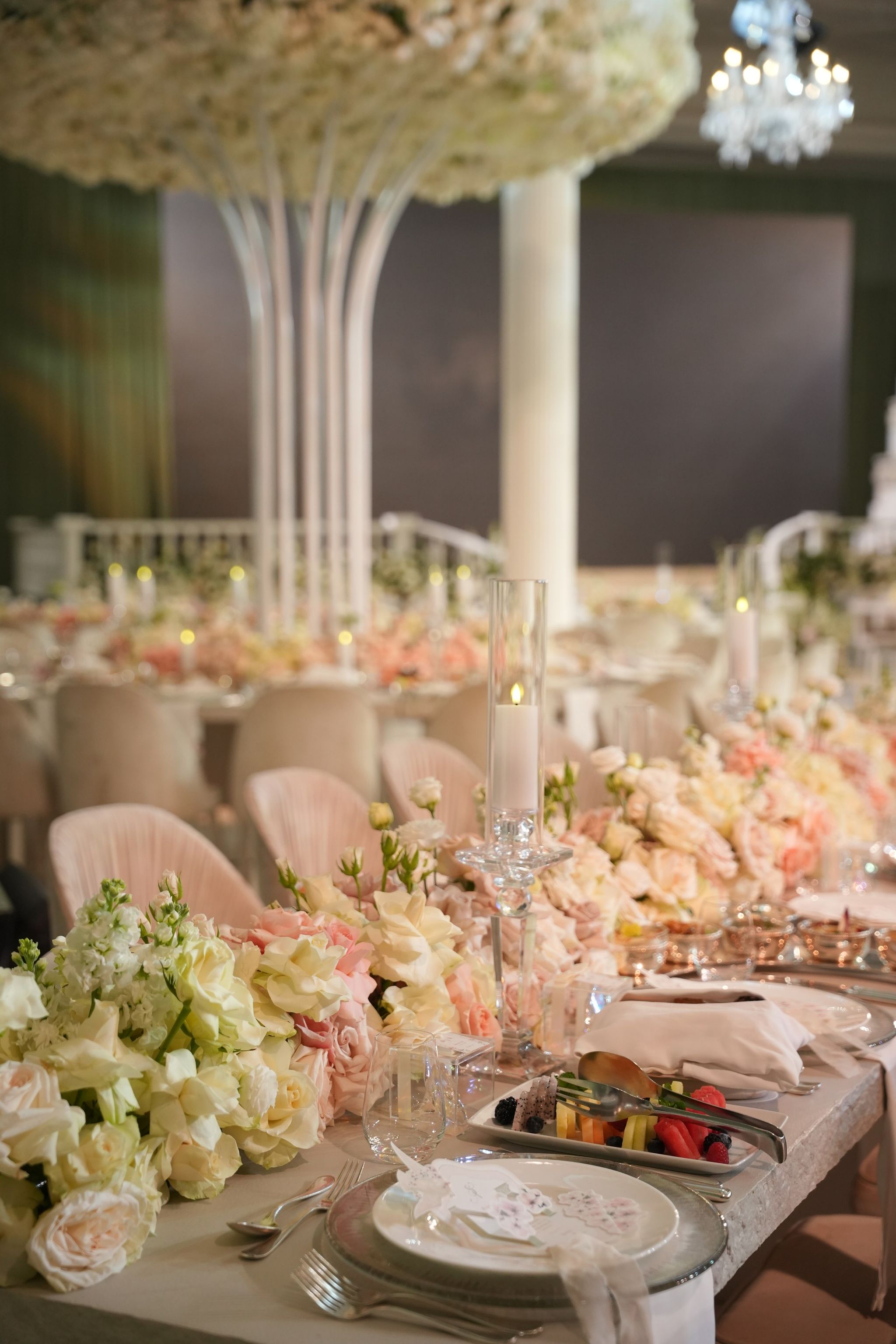 Long table of blush and ivory roses beneath a suspended floral canopy and crystal chandelier