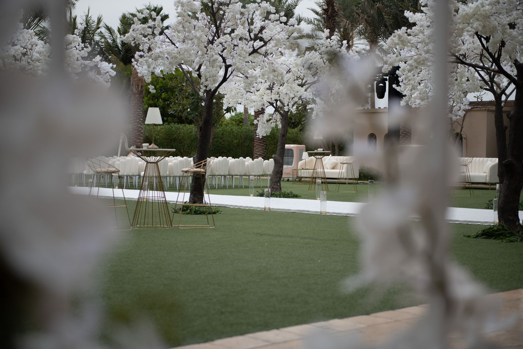 White blossom trees on the lawn among gold high tables and ivory lounge sofas