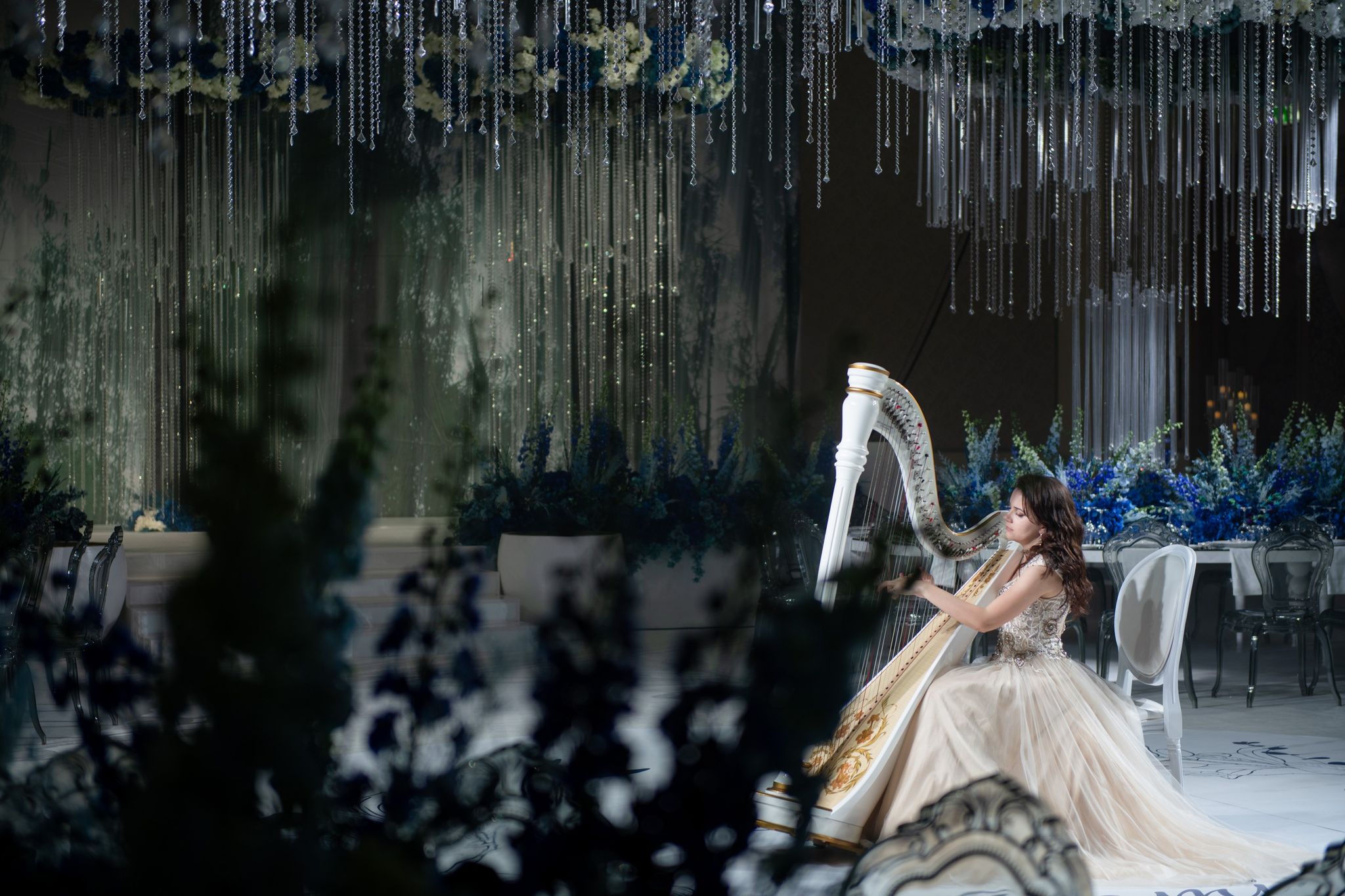 A harpist framed by blurred delphiniums, with crystal curtains and blue centrepieces behind