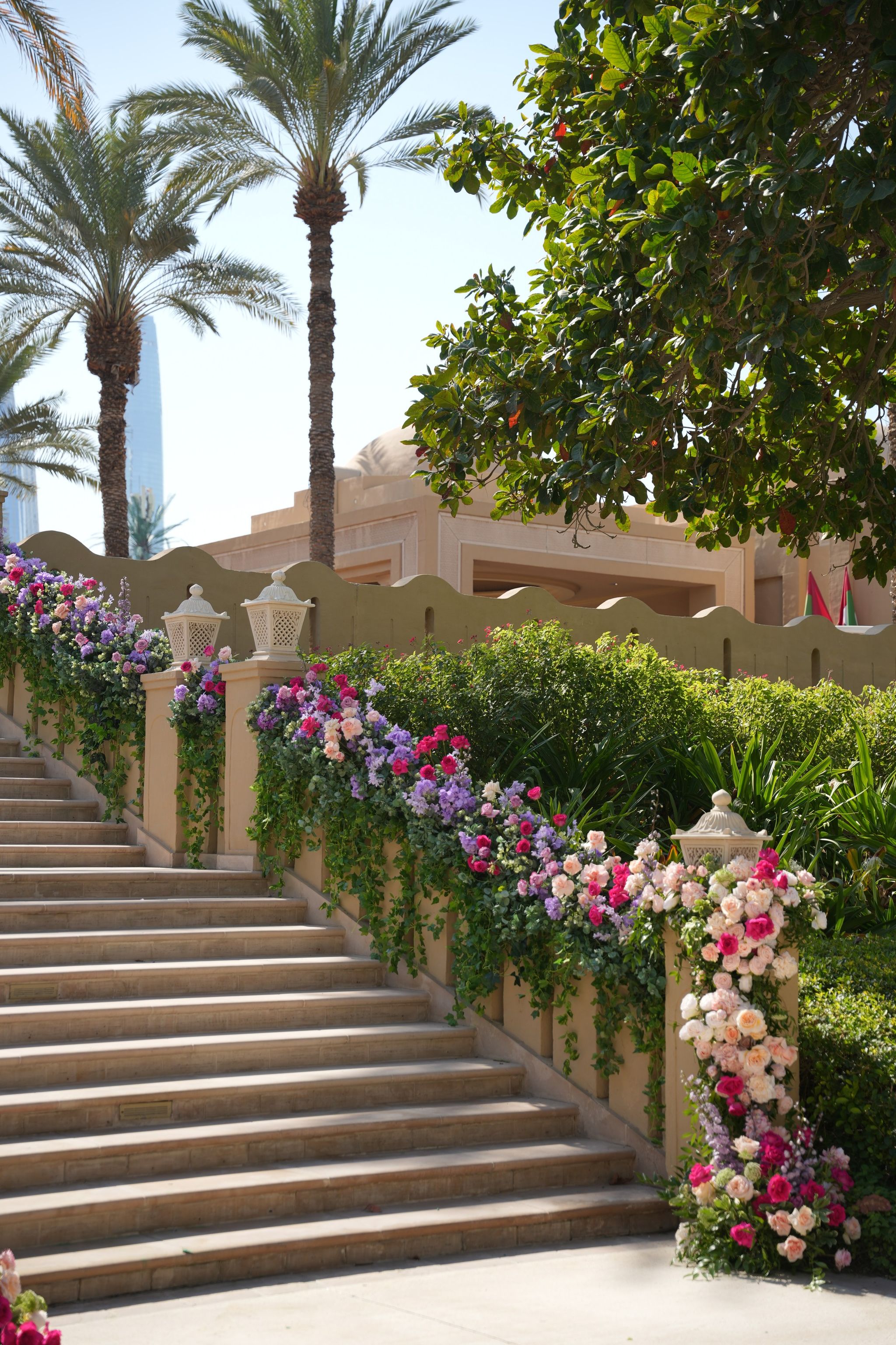 Cascading rose and stock garland along a sandstone balustrade with lanterns and date palms
