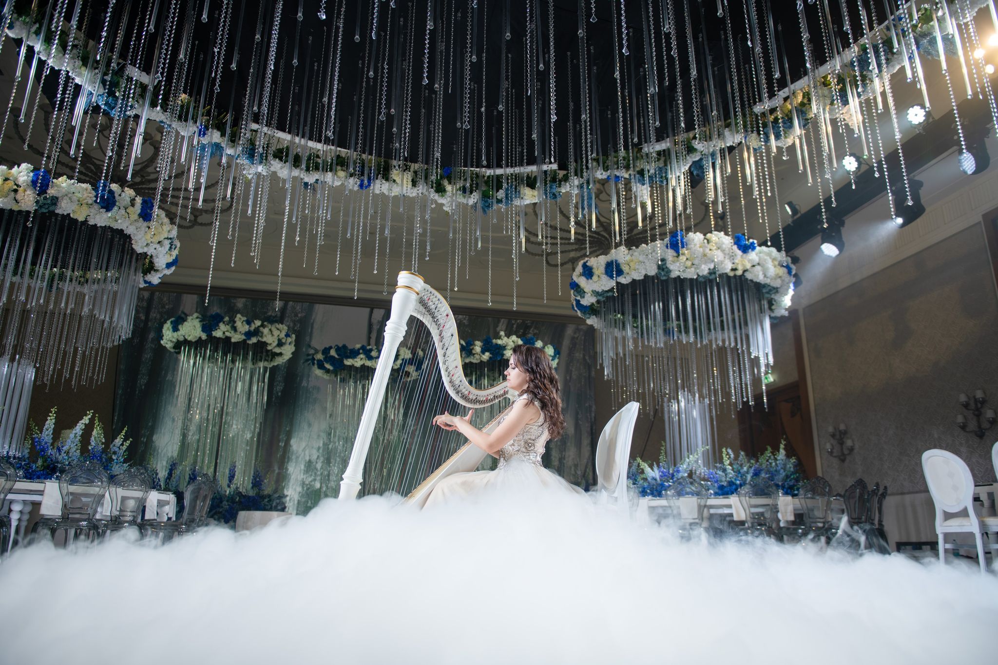 Low-angle view of a harpist in fog under suspended blue and white floral rings