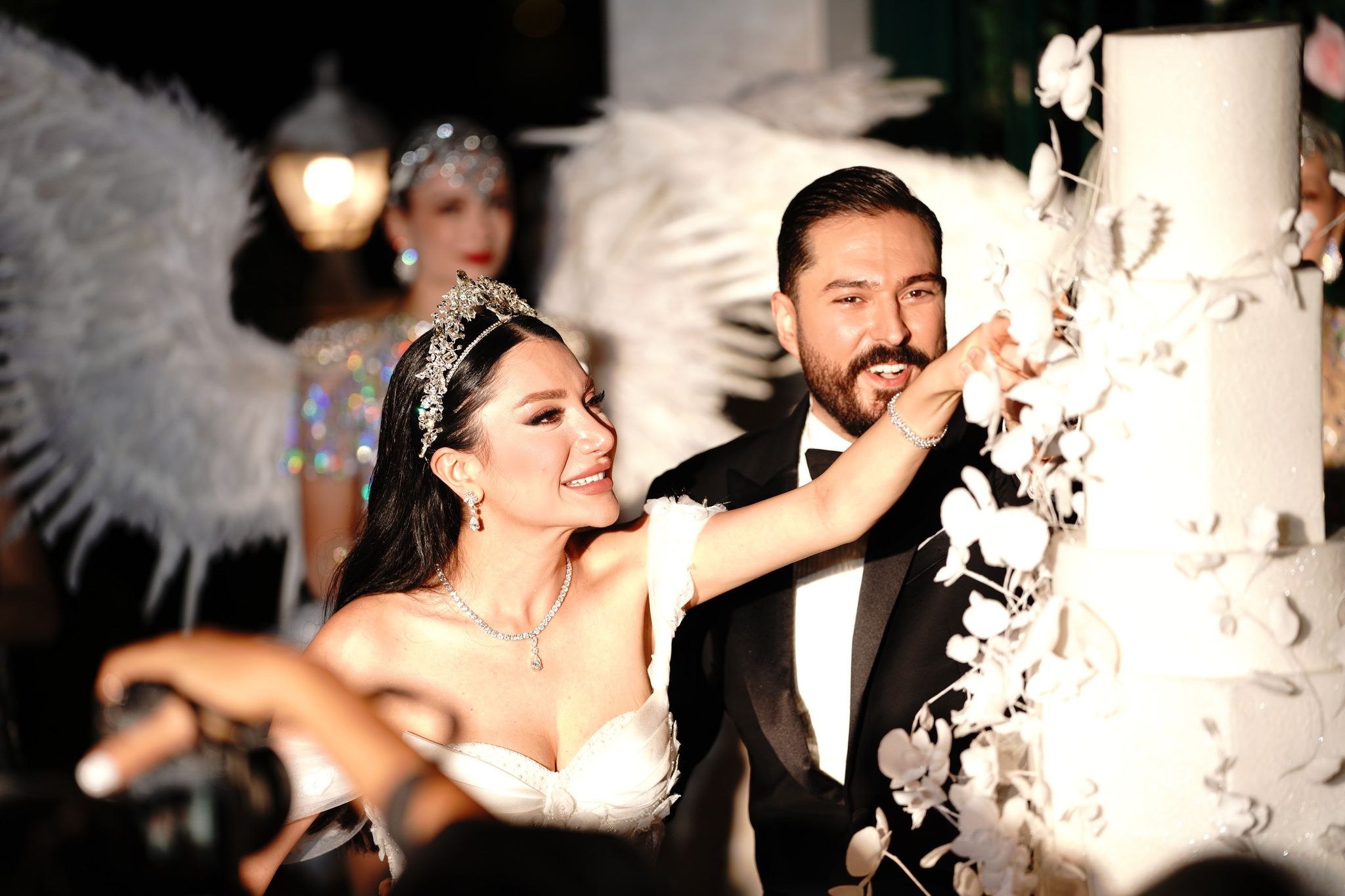 The bride and groom cutting a white cake with sugar flowers, winged dancers behind