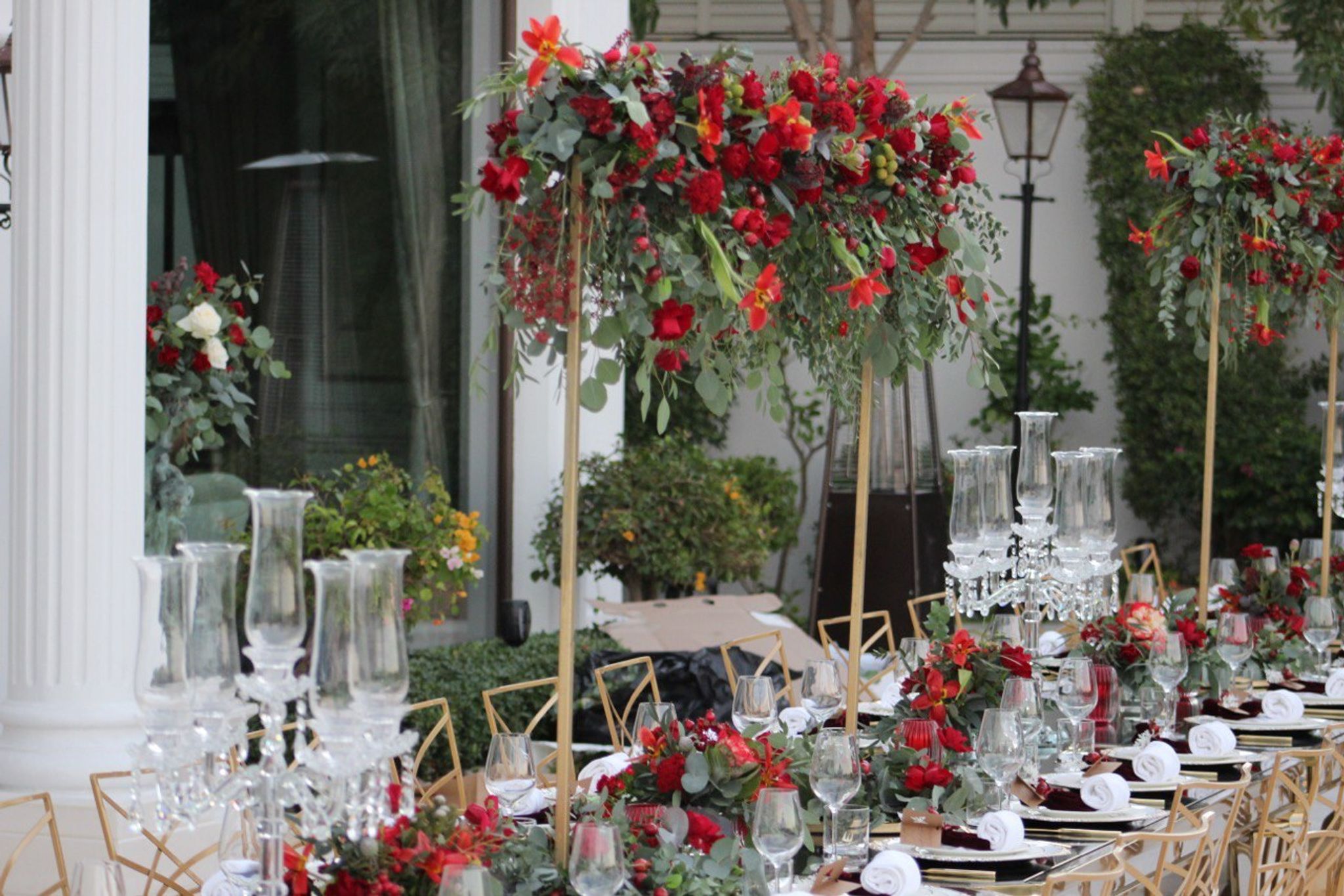 Tall red floral stands and crystal candelabra along a long table set with burgundy napkins