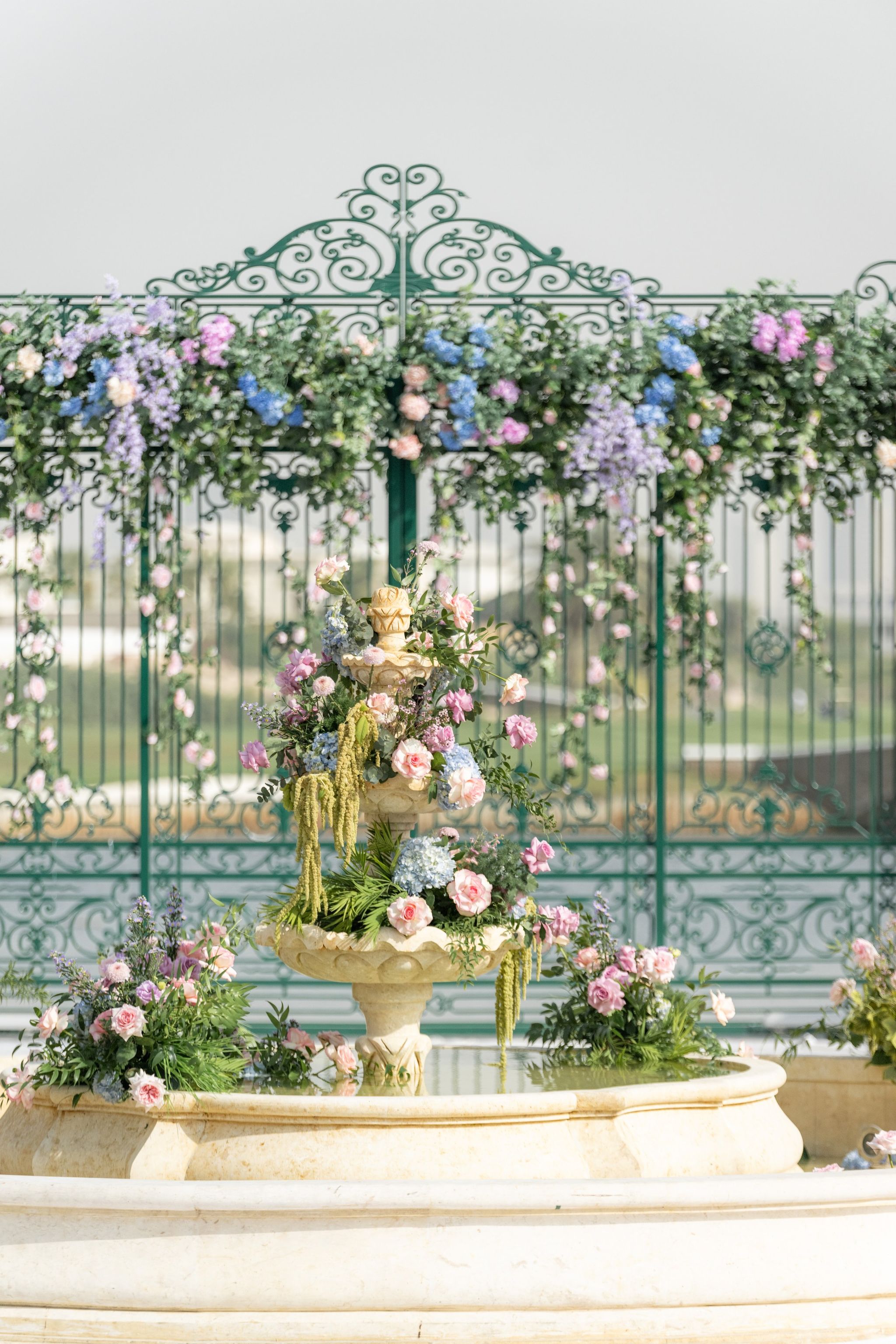 Rose-dressed stone fountain before an ornate green iron gate at Four Seasons Resort Dubai at Jumeirah Beach