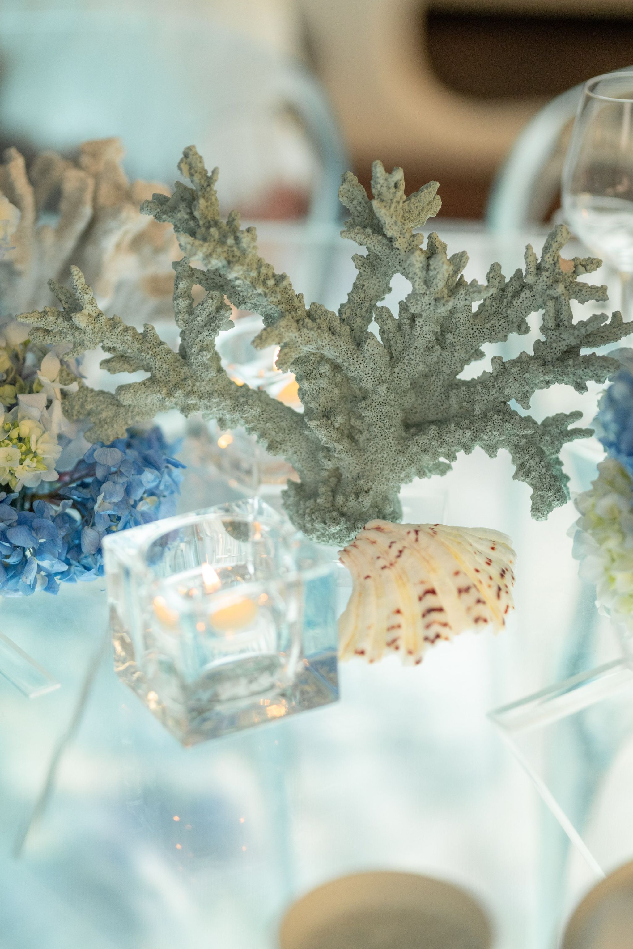 Sea-green coral, a scallop shell and a glass votive among blue hydrangeas