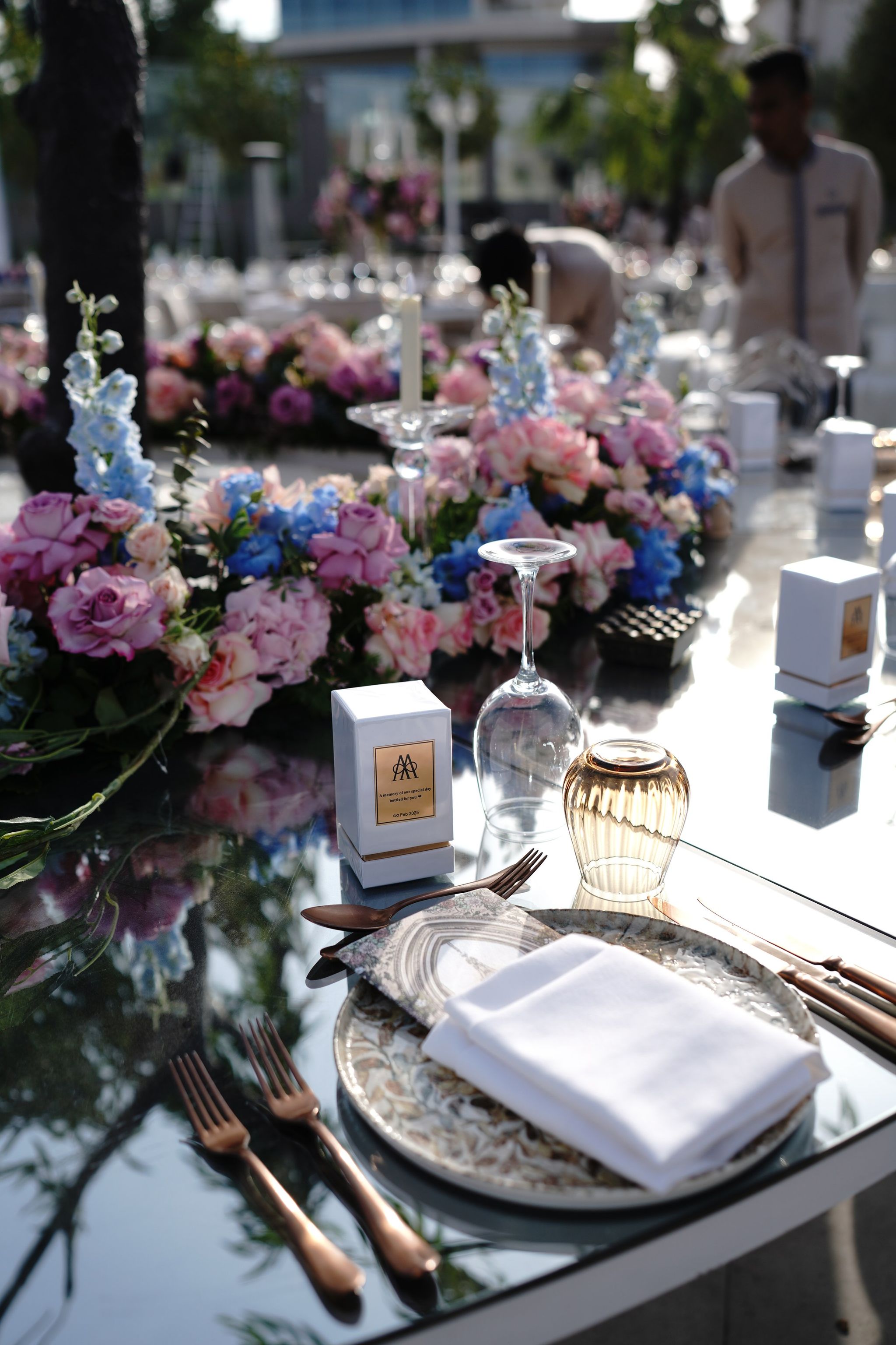 Place setting with bronze cutlery, gold-rimmed plate and a favour box beside a low rose garland