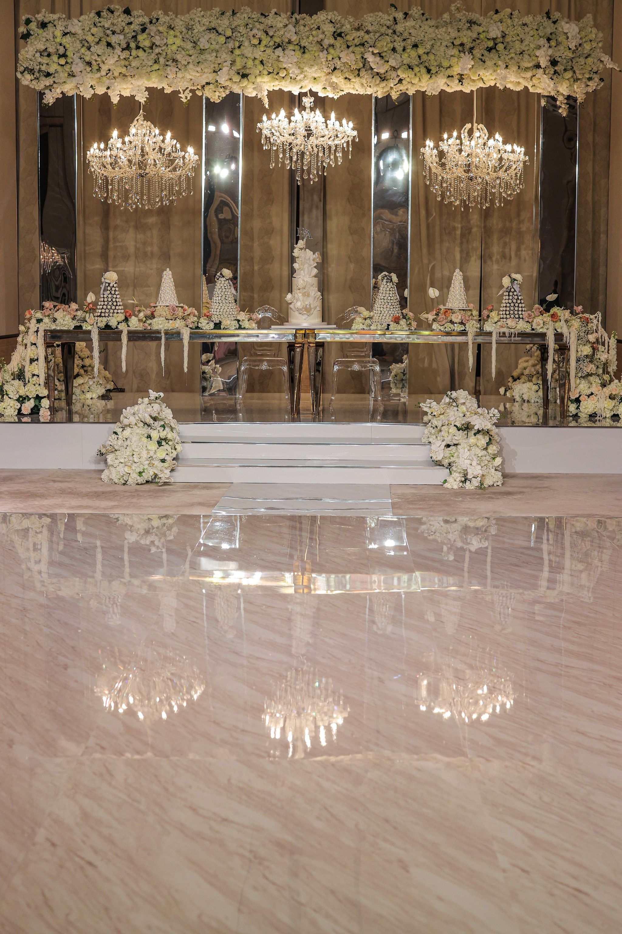 Mirrored stage with three crystal chandeliers, a suspended ivory floral canopy and croquembouche towers