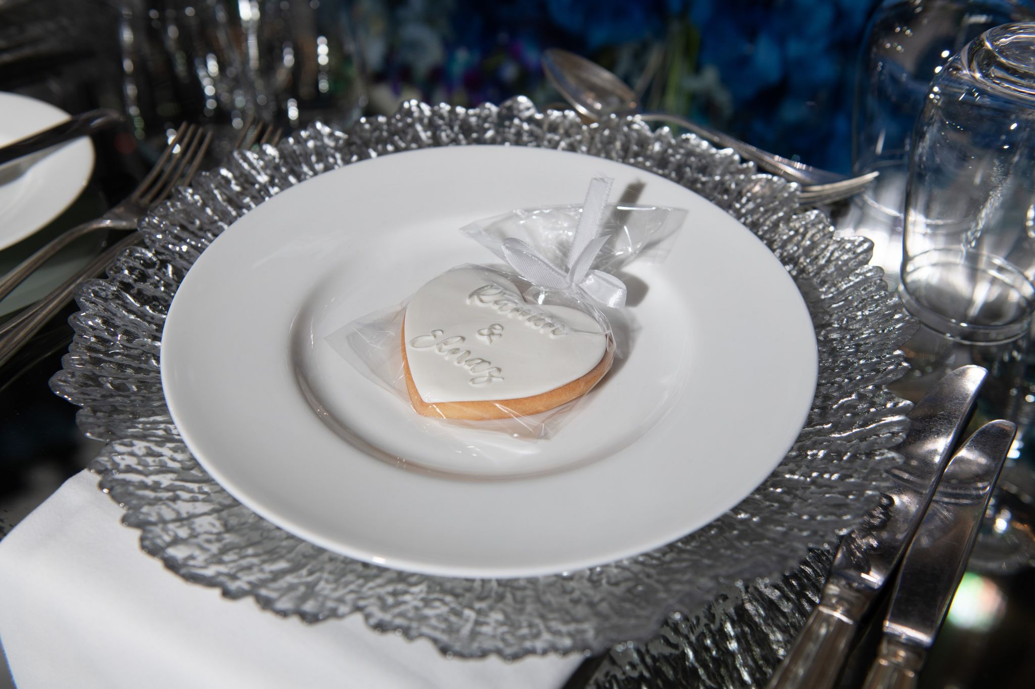 Heart-shaped iced biscuit favour wrapped in cellophane on a white plate and silver charger