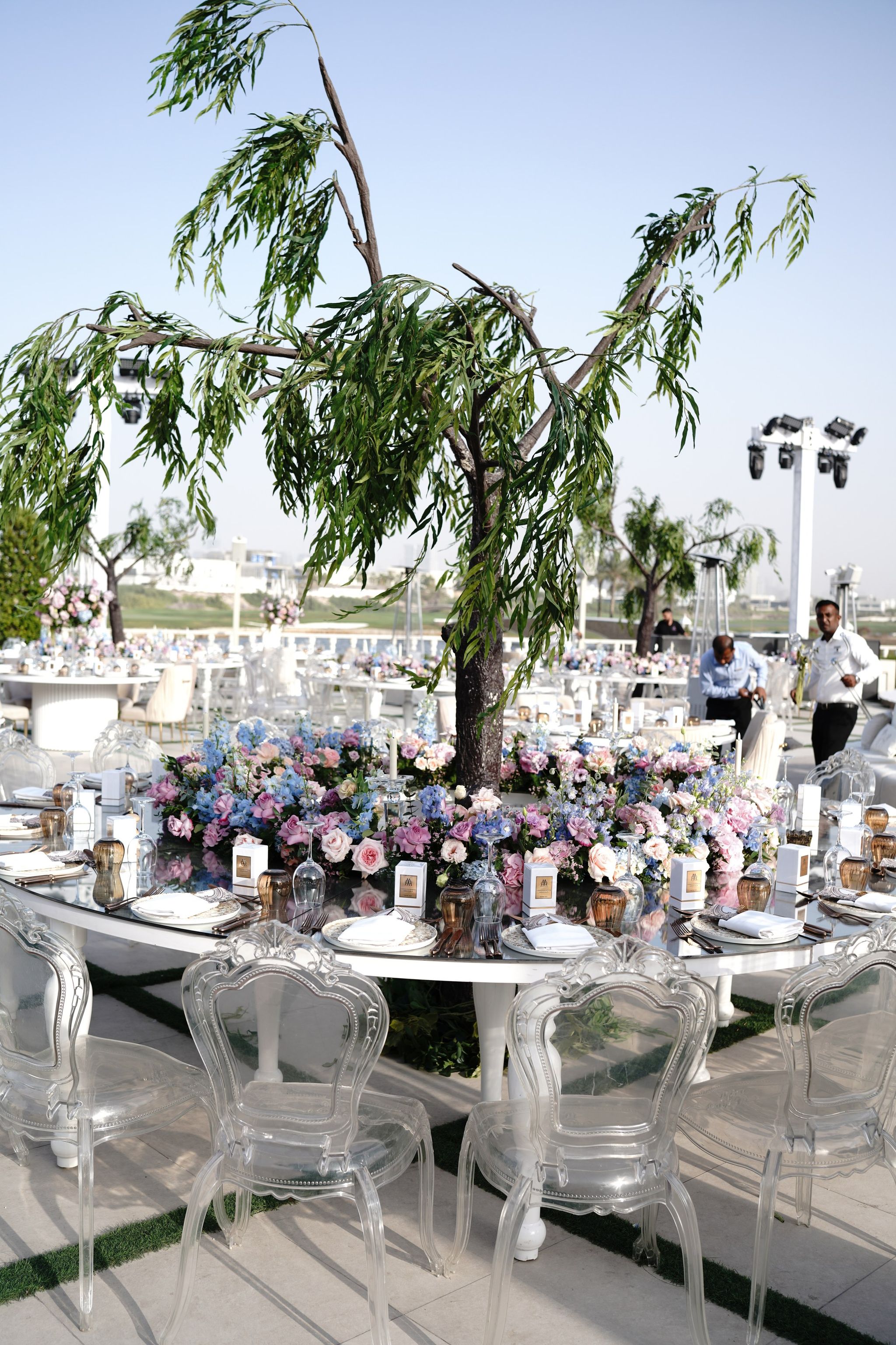 Weeping tree centrepiece rising from hydrangea and roses on a round table with ghost chairs