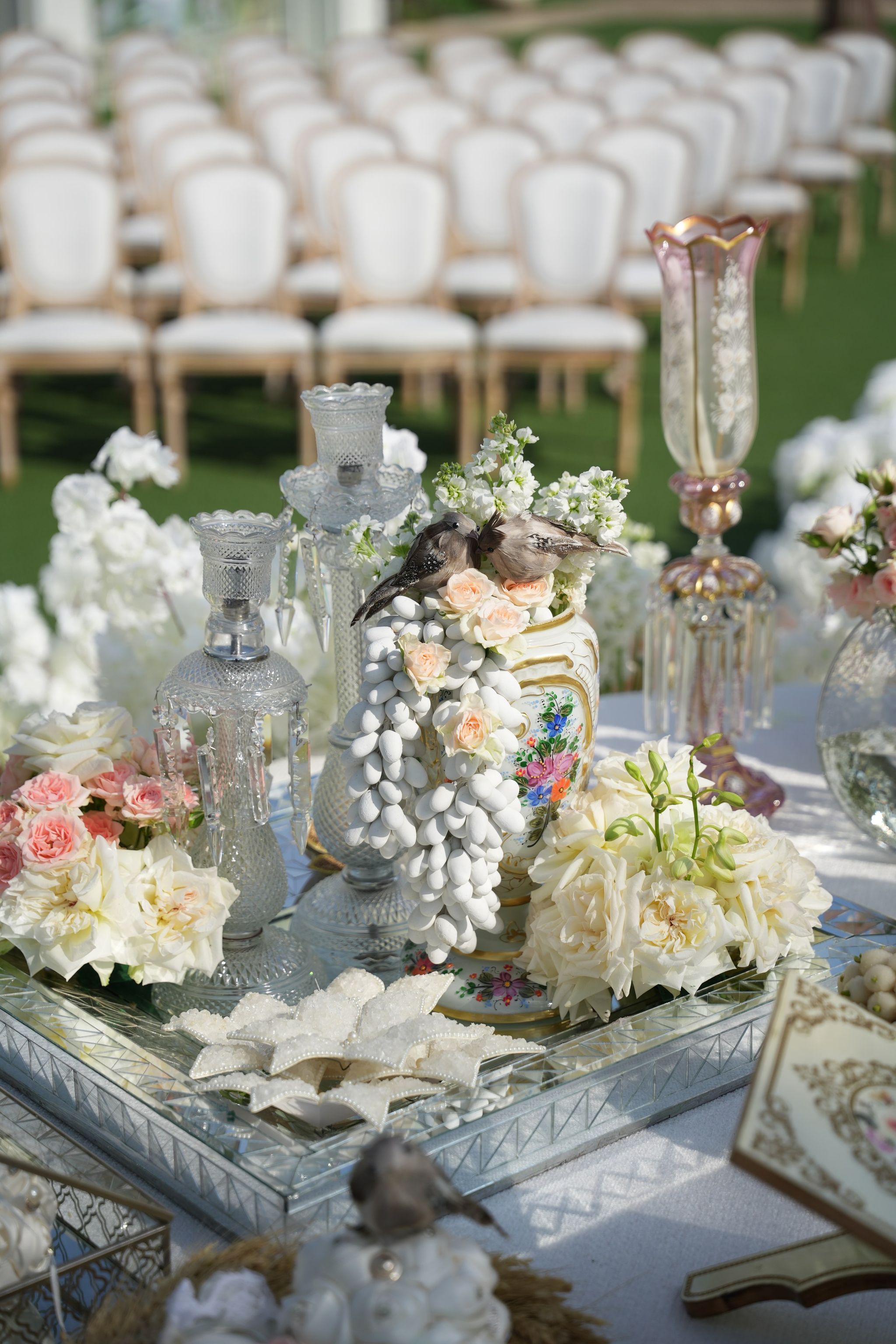 Sugared-almond tower topped with bird figurines among crystal decanters, peonies and pink roses on a mirrored tray