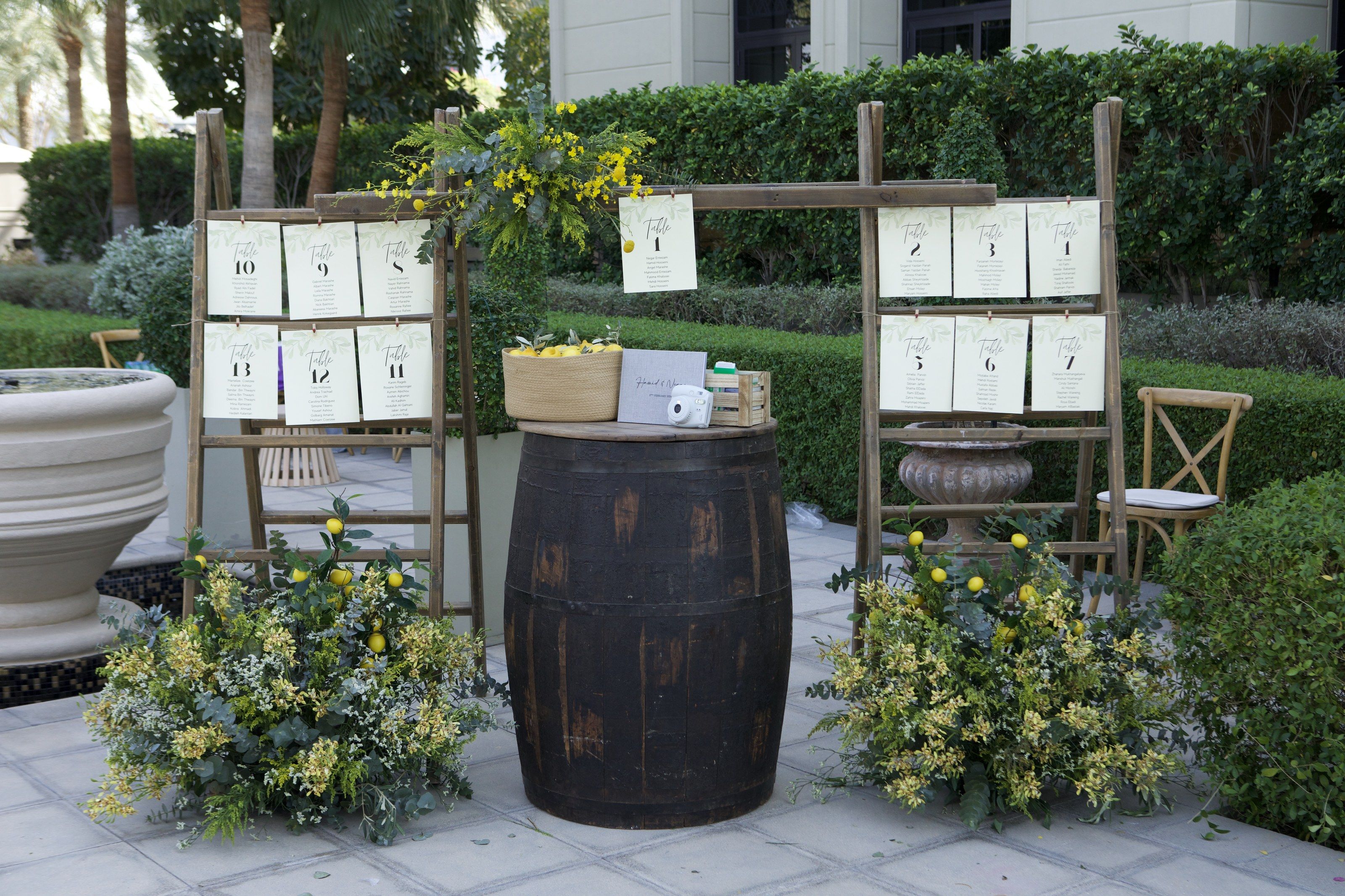 Seating plan hung on timber ladders beside a wine barrel, with mimosa and lemon arrangements