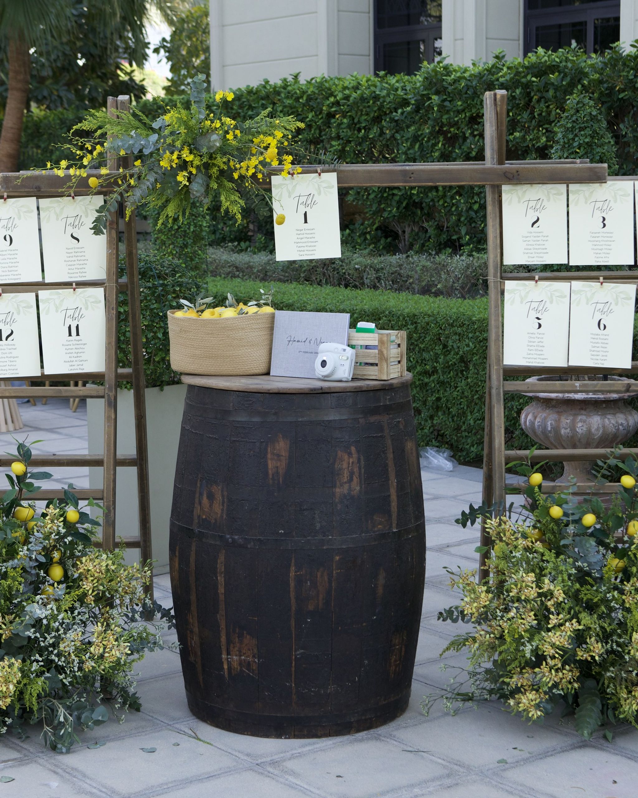 Seating plan hung on timber ladders beside a wine barrel, with mimosa and lemon arrangements