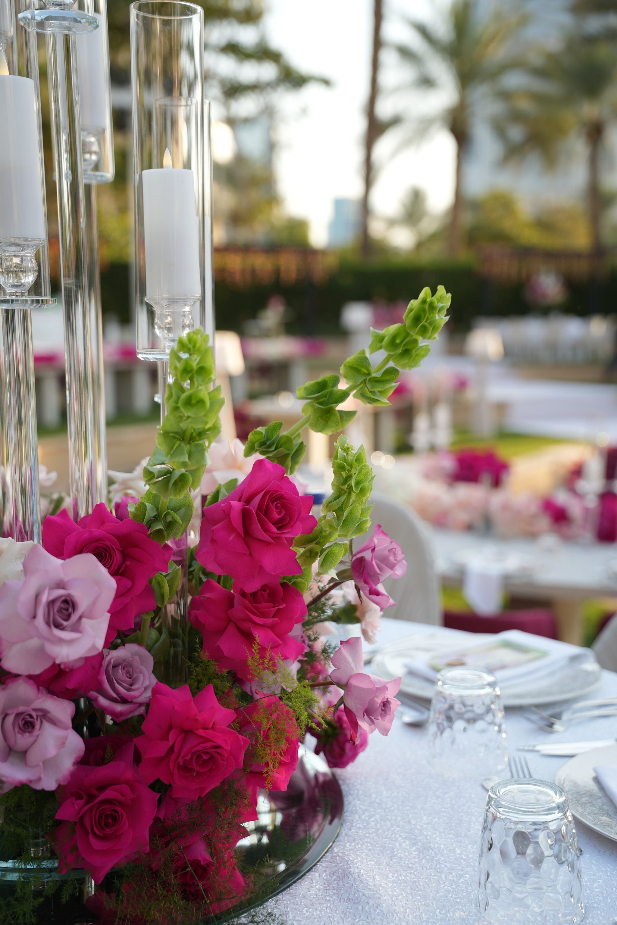 Fuchsia and lilac roses with bells of Ireland beside cut-crystal glasses on a shimmering cloth