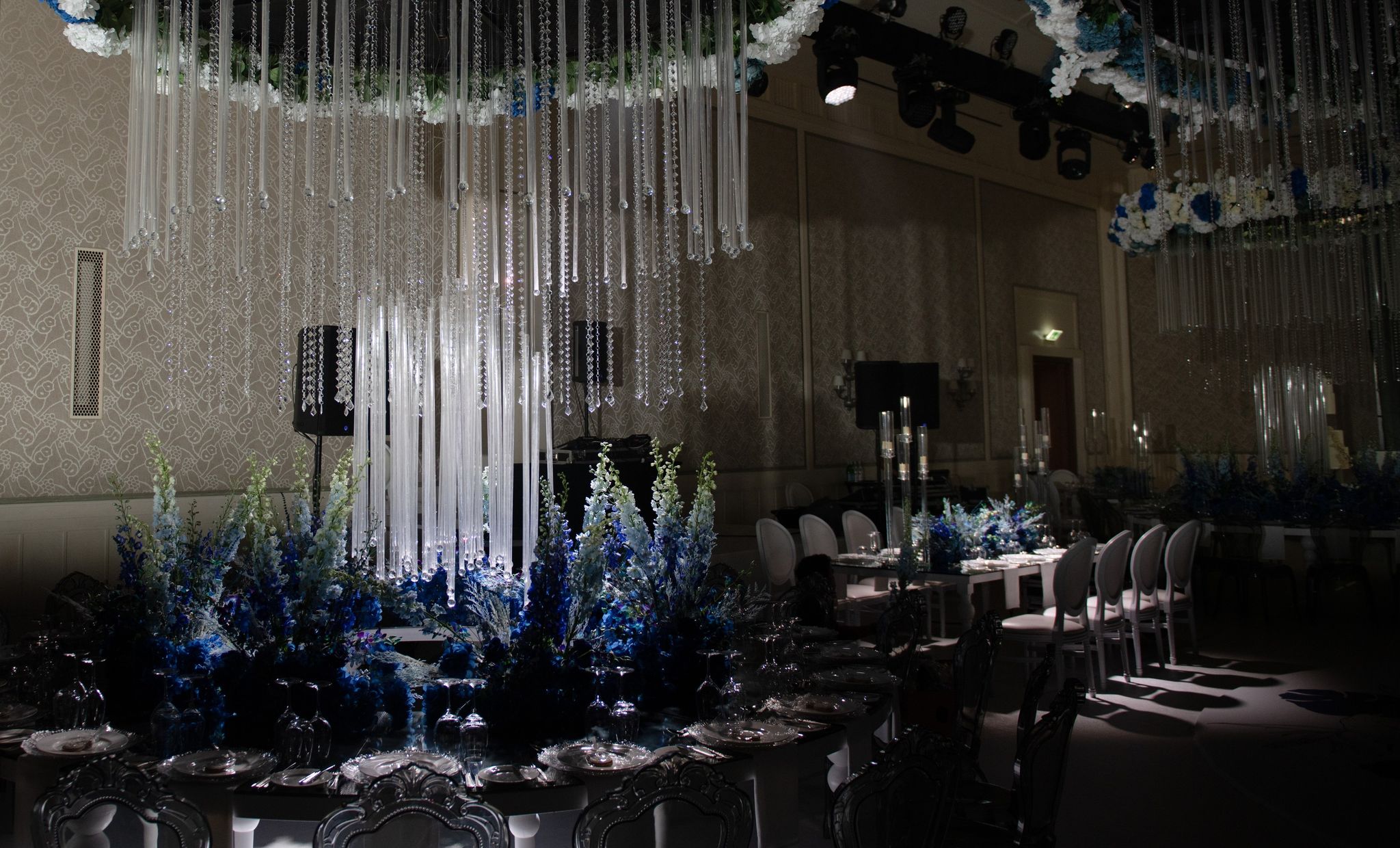 Spotlit crystal strands falling over blue delphinium centrepieces in the darkened ballroom