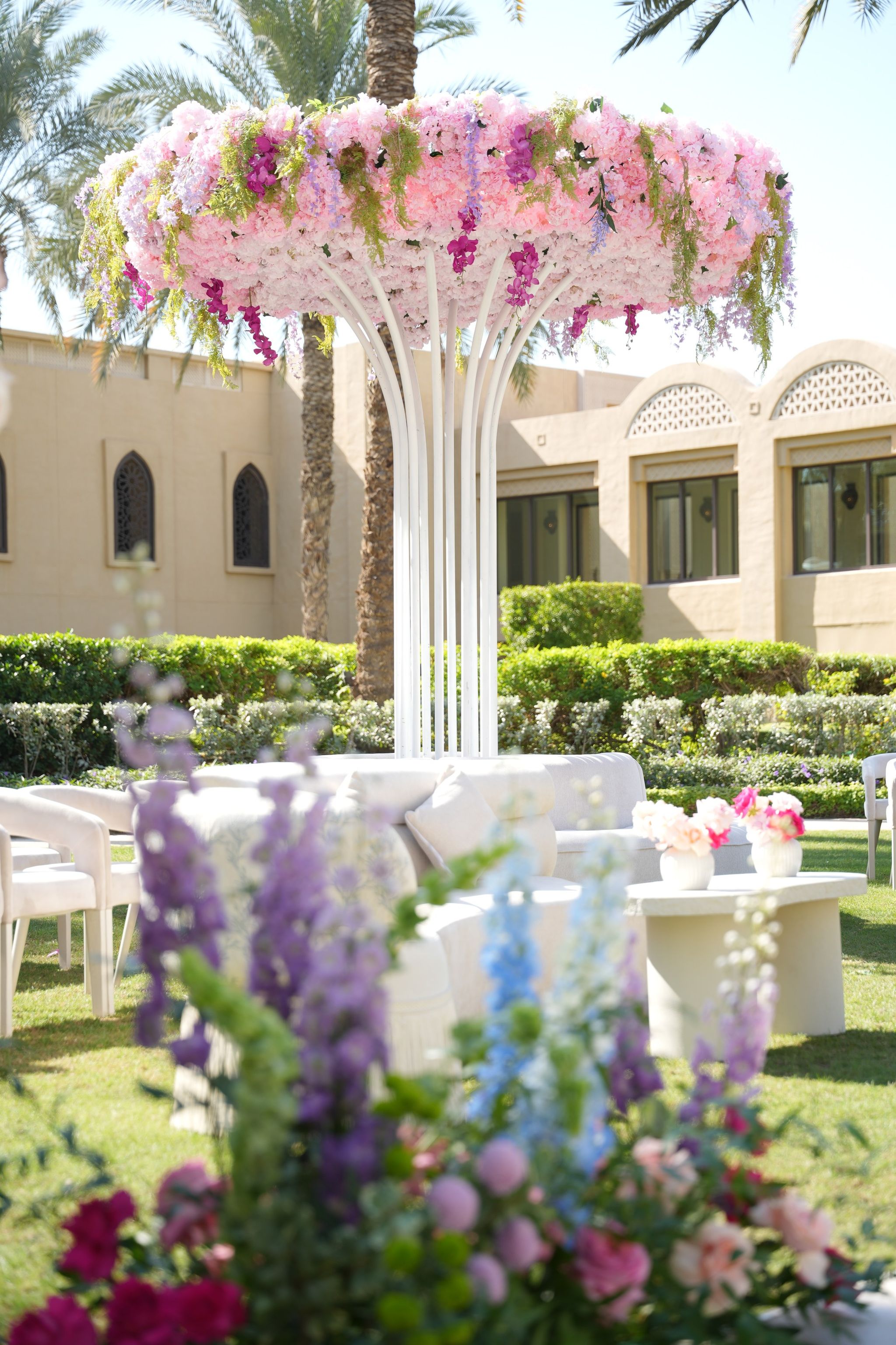 Floral canopy of pink hydrangea and orchids over a lounge, framed by purple delphiniums