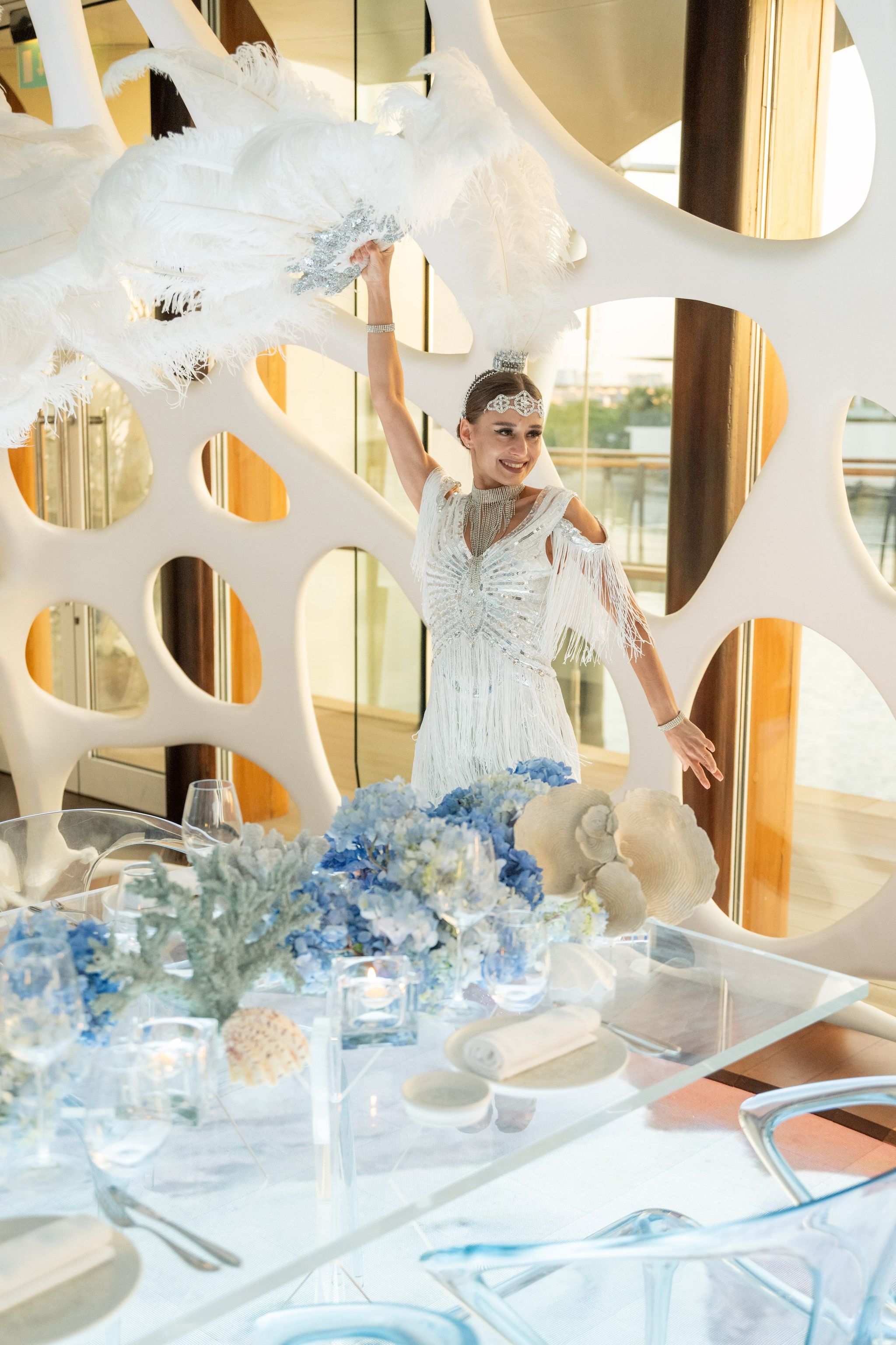Performer in silver fringe raising a white feather fan behind the hydrangea tablescape