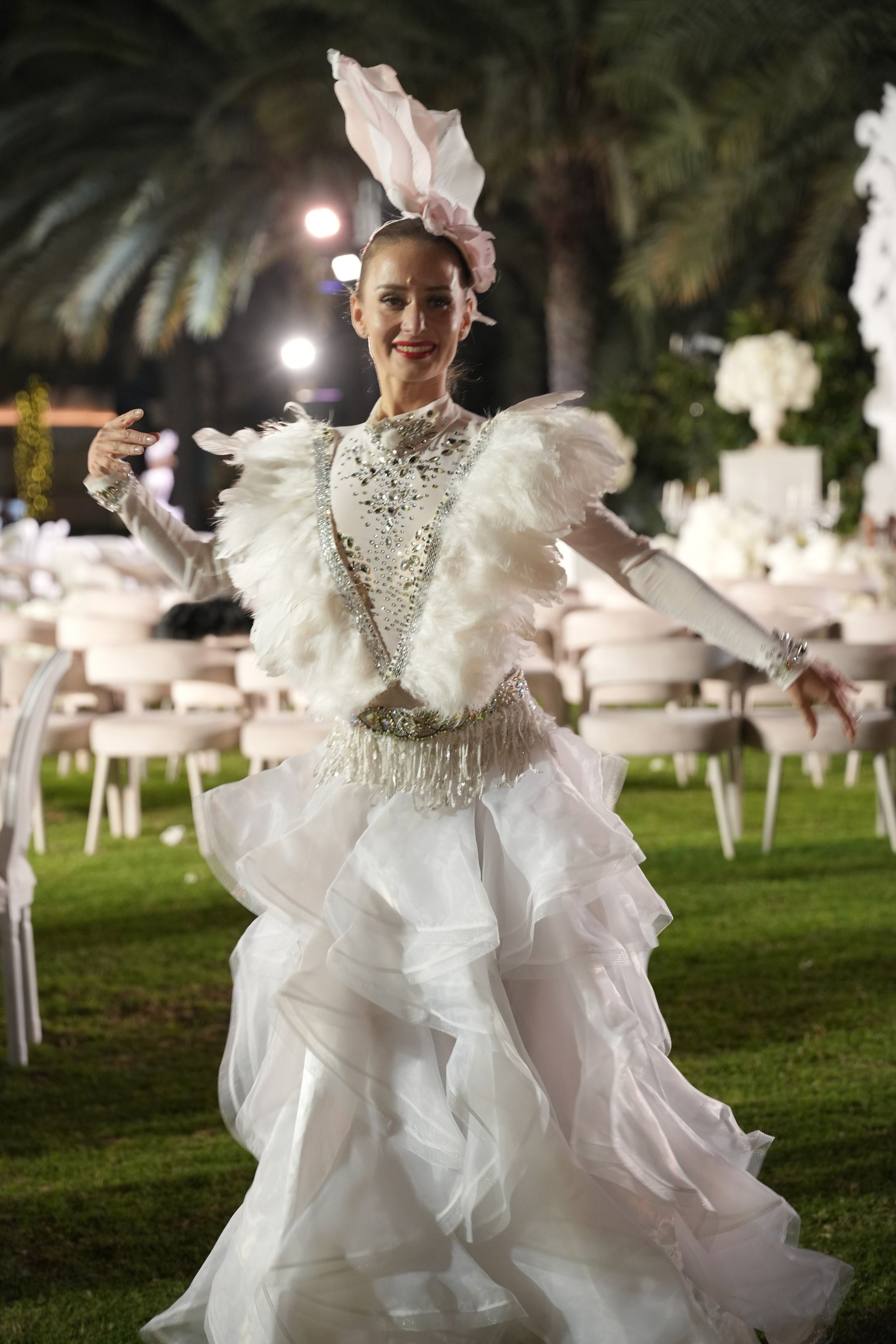 A performer in a feathered white bodice and ruffled organza skirt dancing on the lawn at night