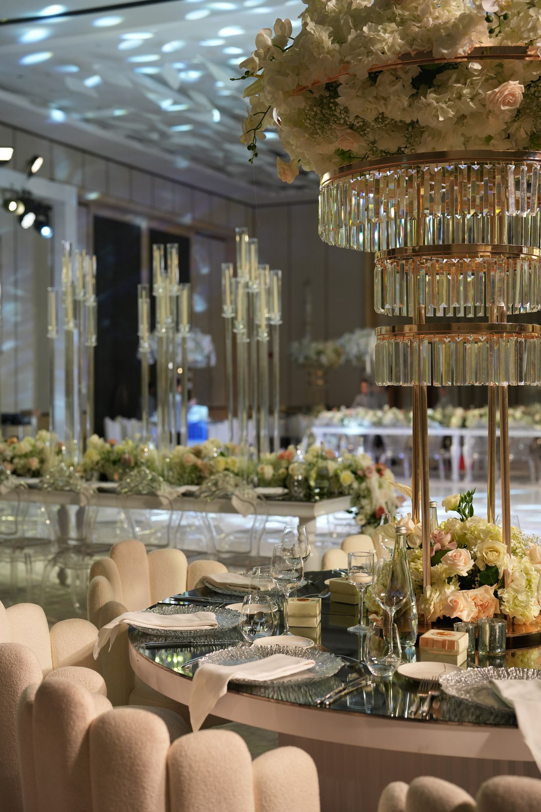Mirrored round table with scalloped ivory chairs beneath a crystal-tiered floral centrepiece
