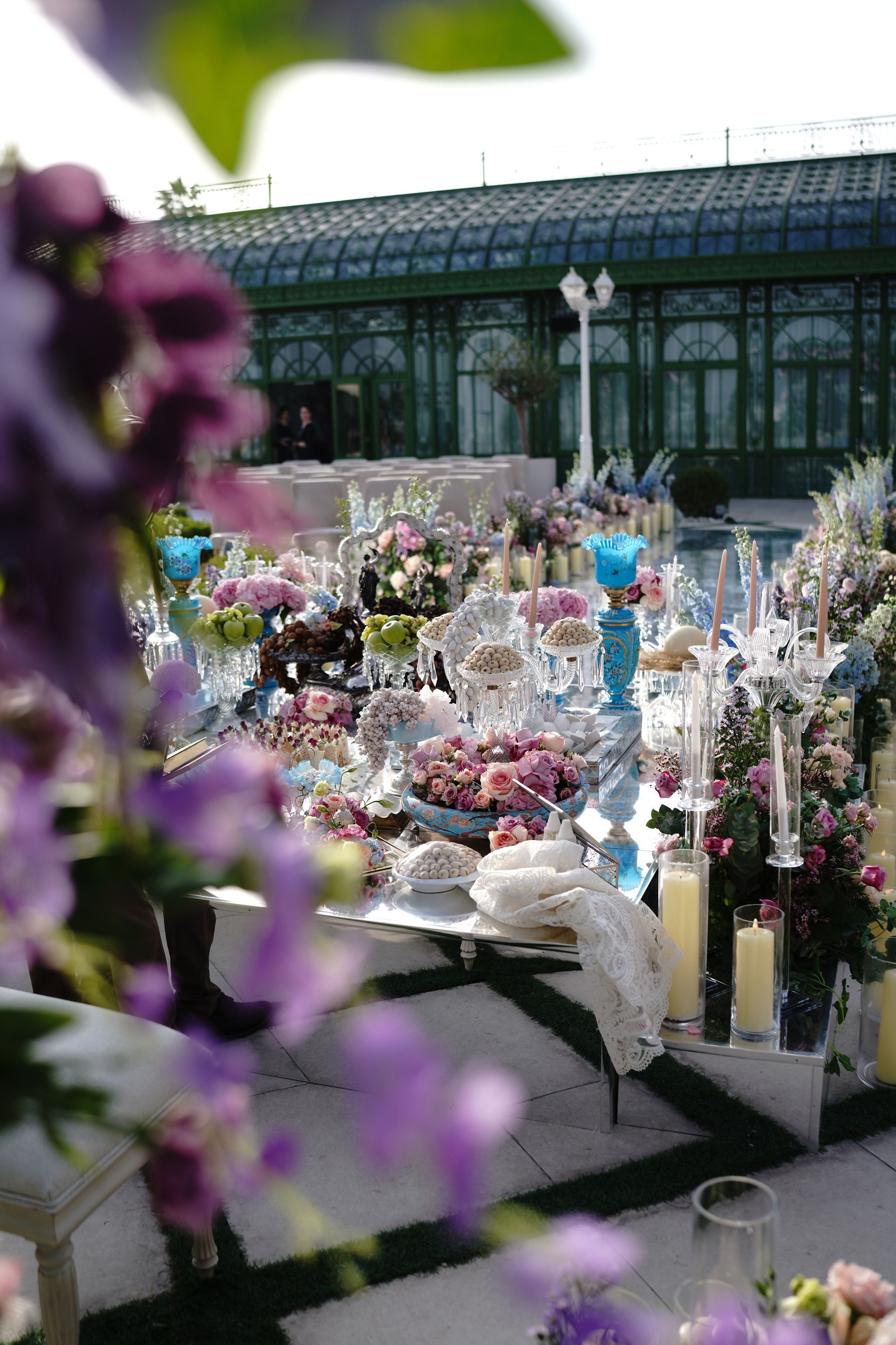 Mirrored sofreh table set with sweets, turquoise vases, candelabra and pastel roses beneath wisteria