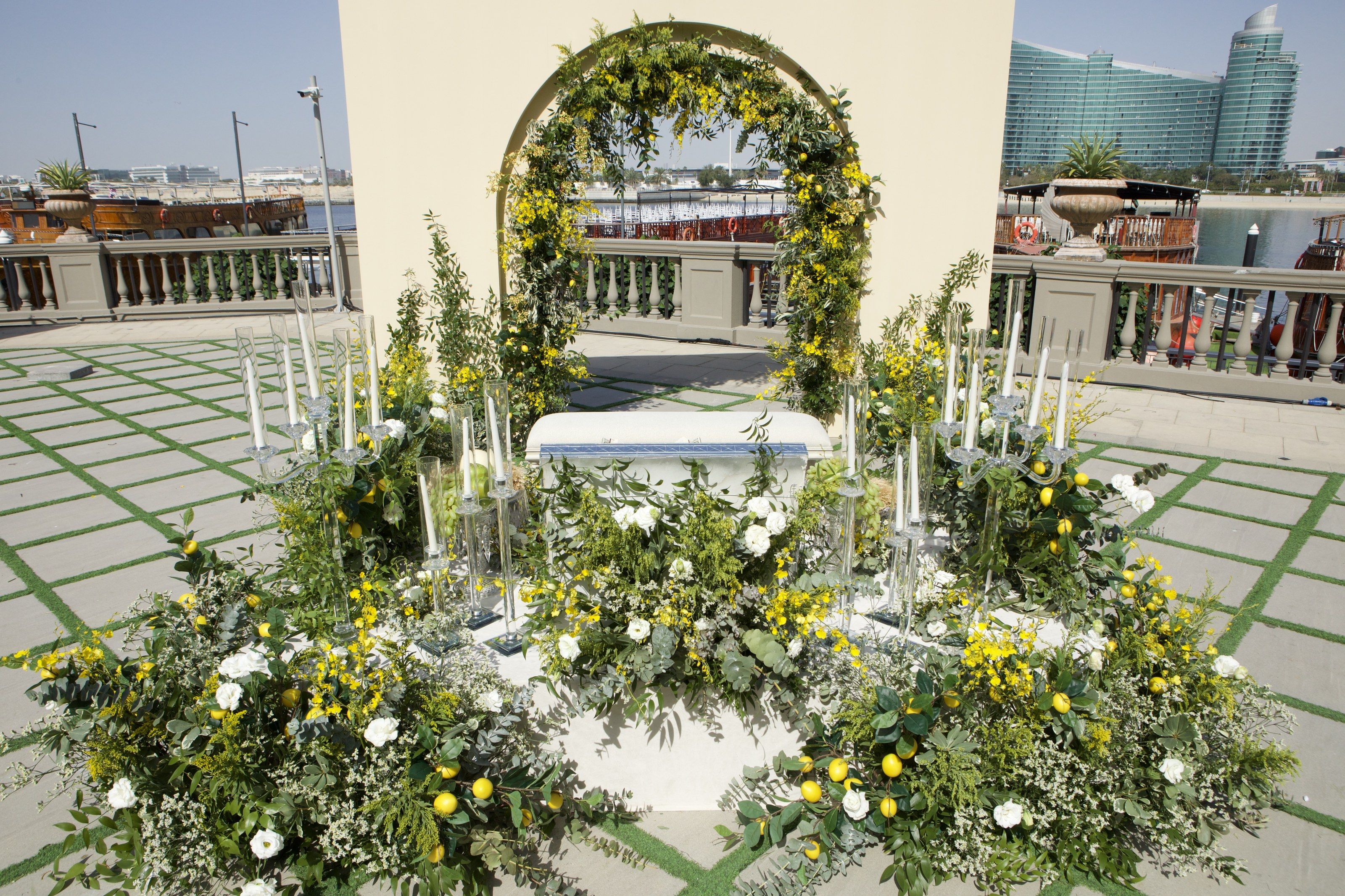 Arch of mimosa and lemon branches above a white ceremony table on the waterfront terrace at Palazzo Versace Dubai