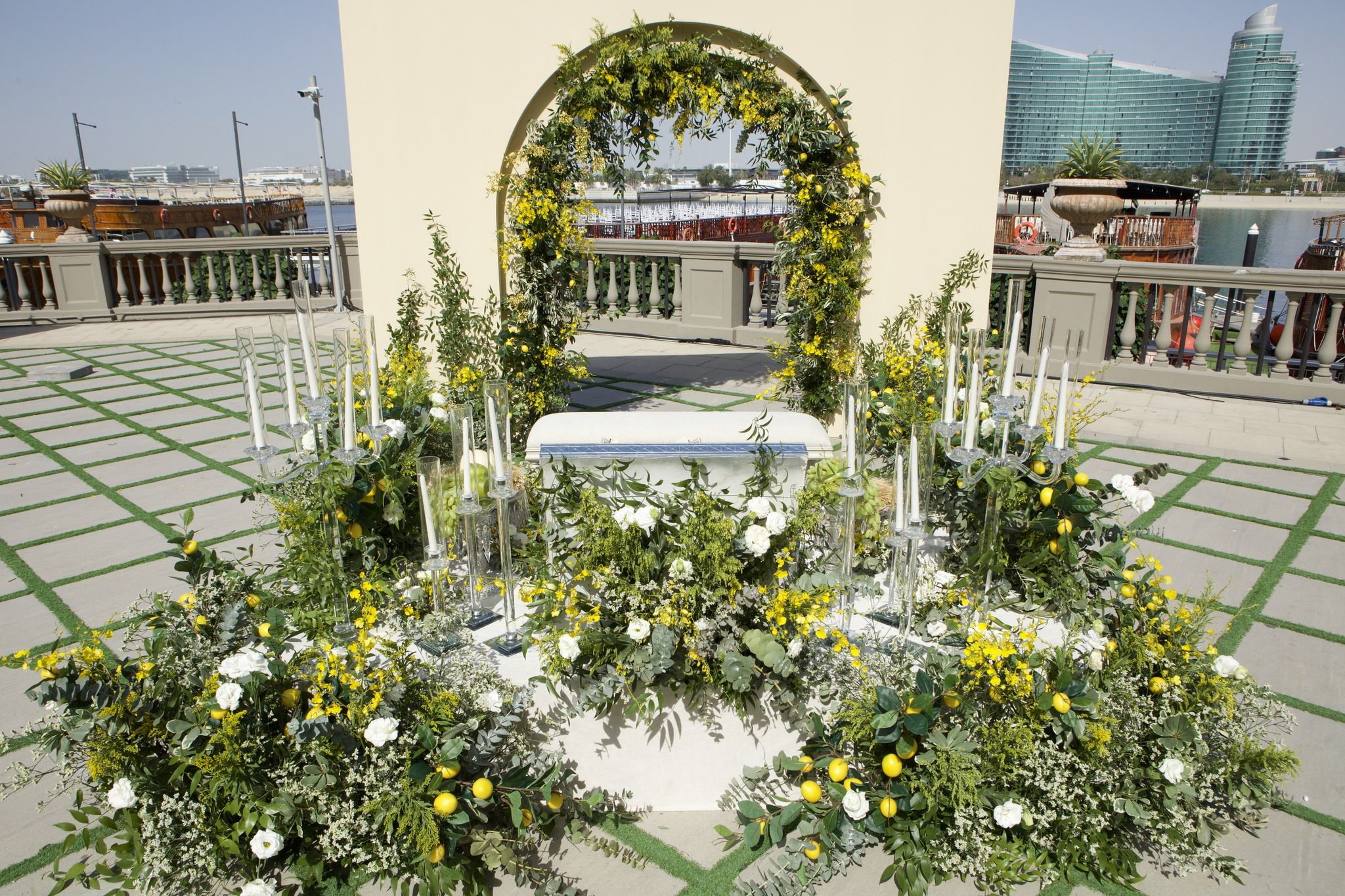 Arch of mimosa and lemon branches above a white ceremony table on the waterfront terrace at Palazzo Versace Dubai