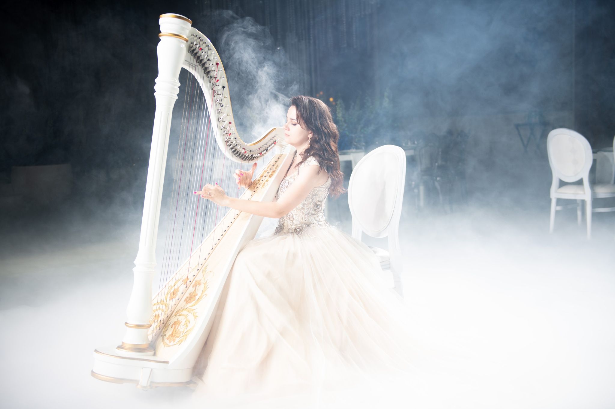 A harpist in a blush gown playing a gilded harp as fog drifts across the ballroom