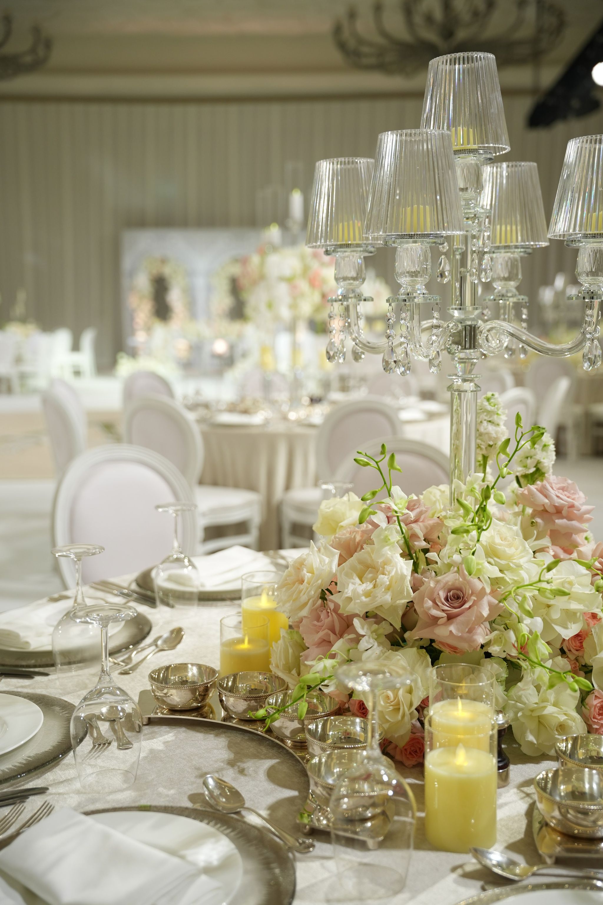 Close view of a shaded candelabra above blush roses, white orchids and glowing pillar candles