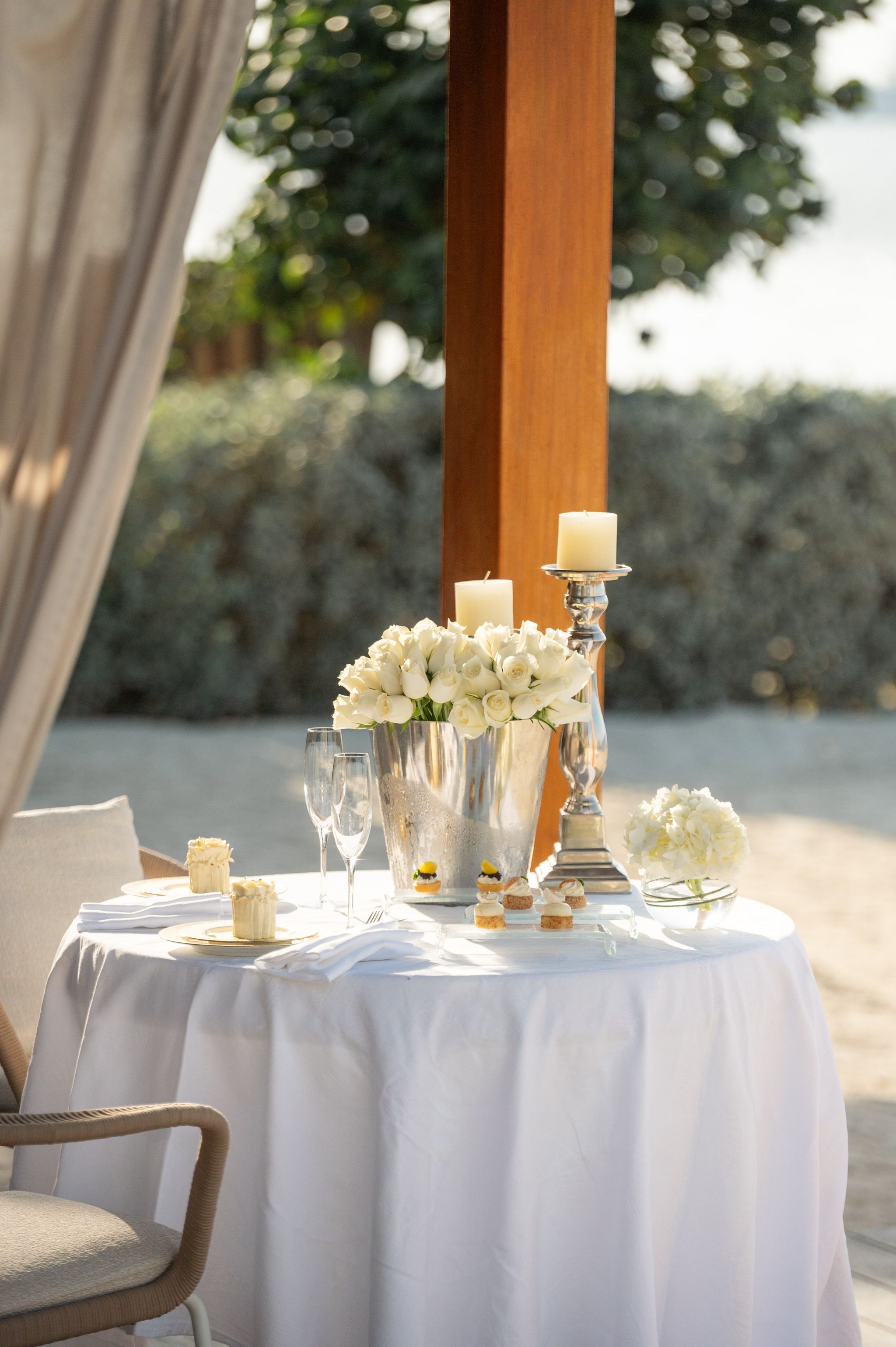 Table for two under the cabana with white roses in a silver bucket and pillar candles