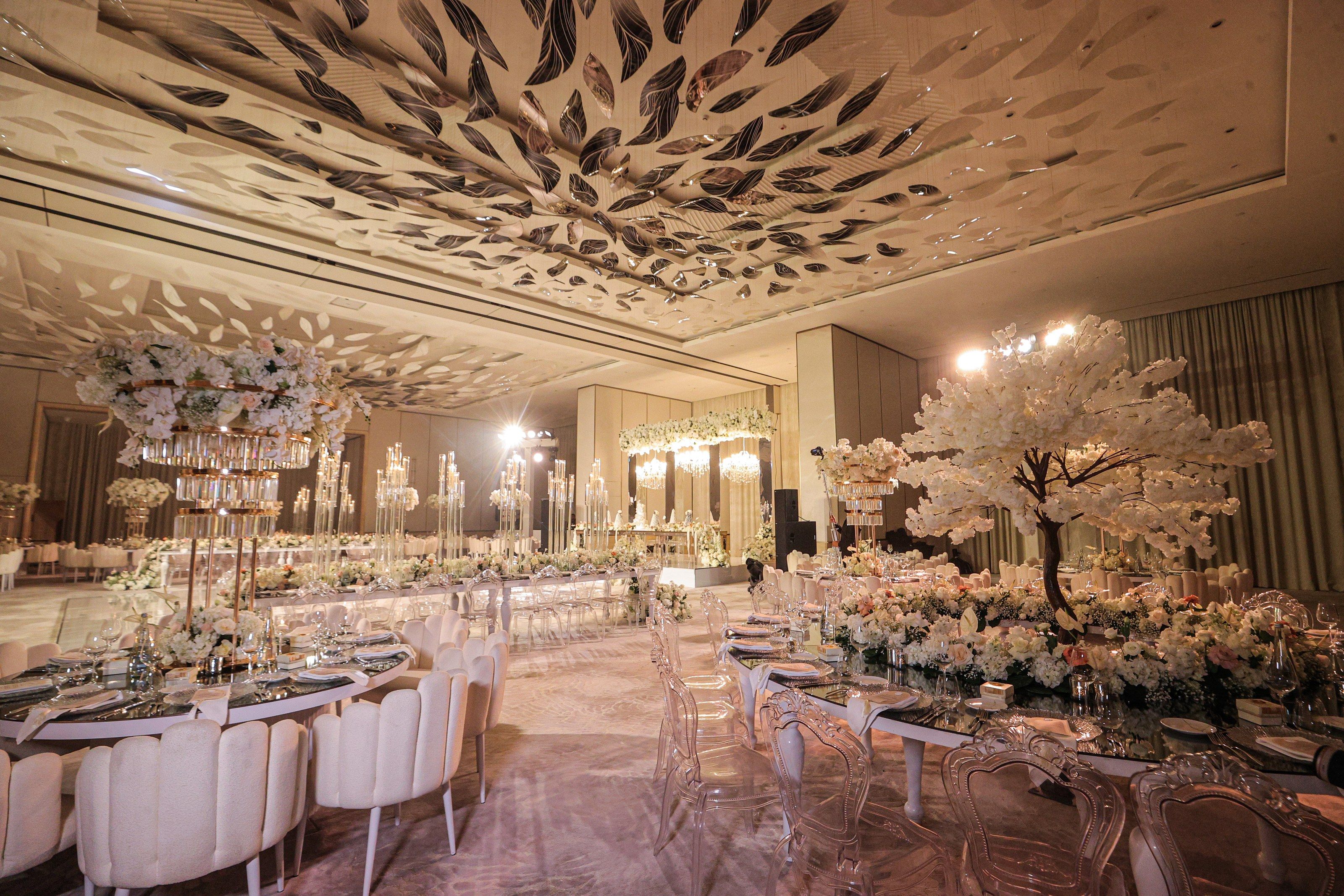 Reception tables with a white blossom tree, crystal-tiered centrepieces and candelabra leading to the stage