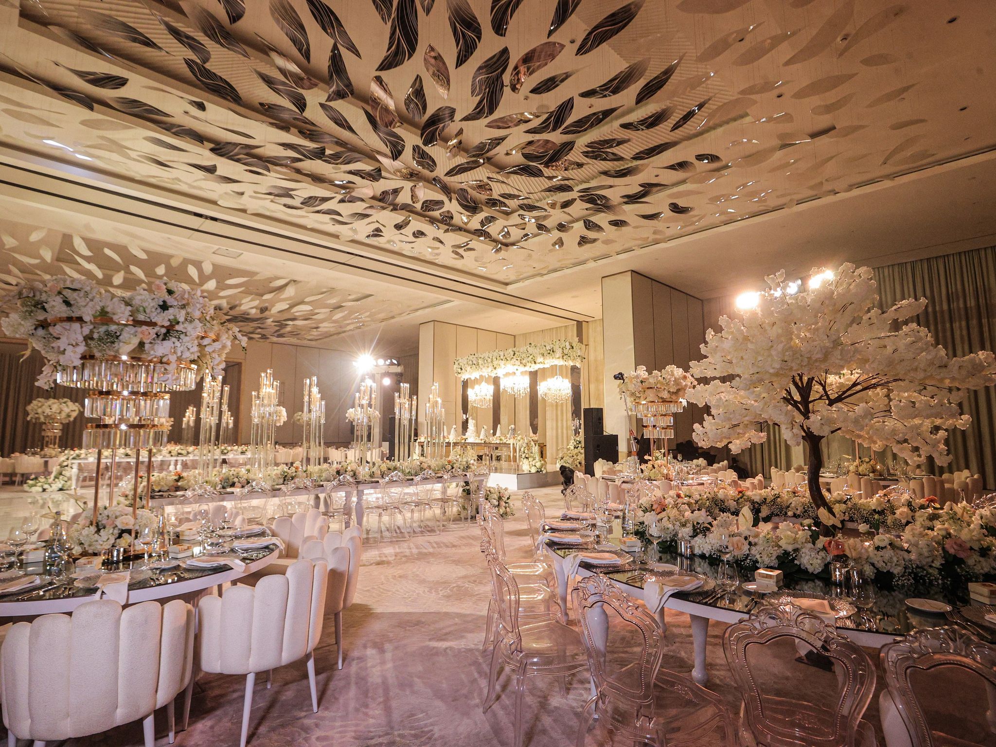 Reception tables with a white blossom tree, crystal-tiered centrepieces and candelabra leading to the stage