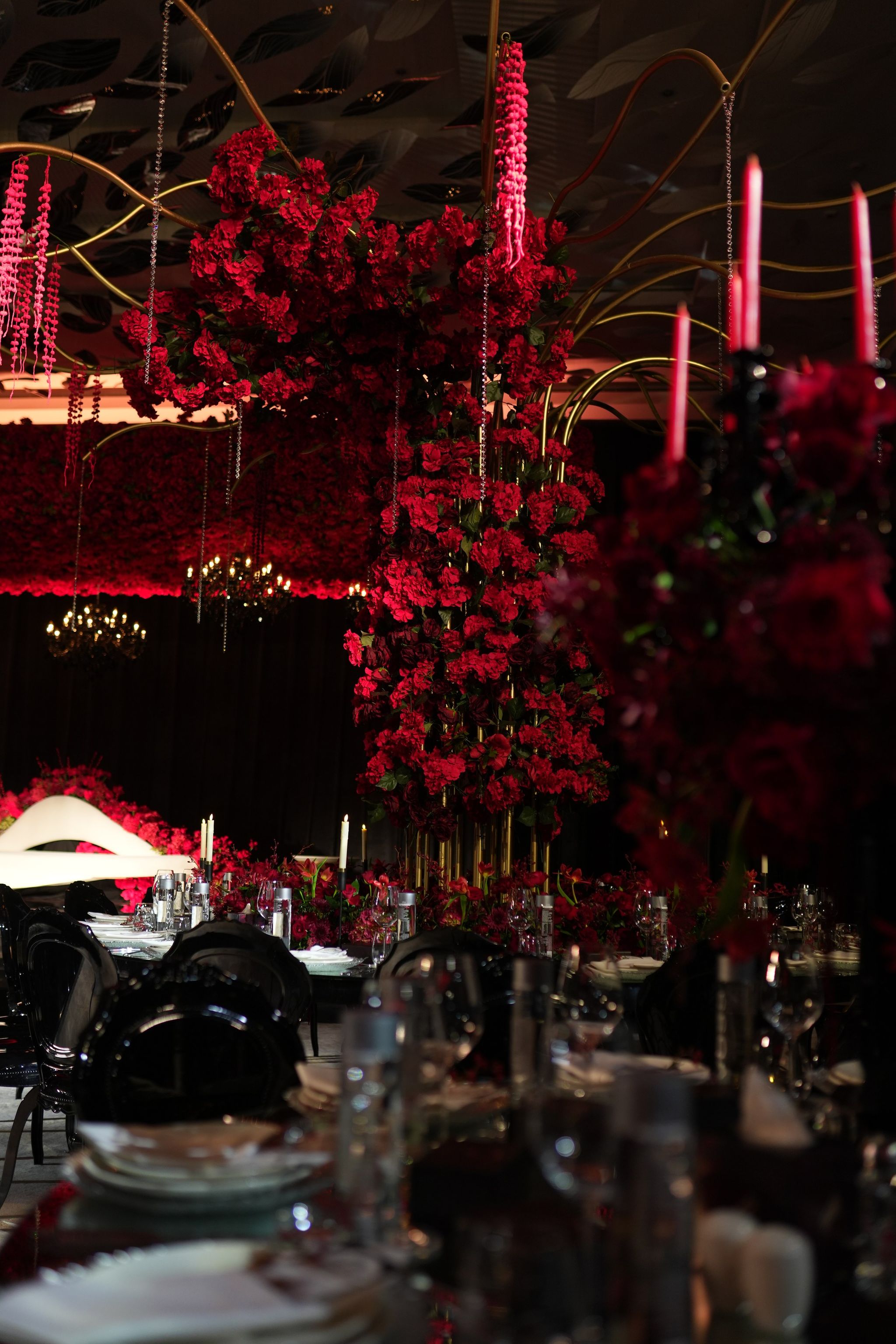 Suspended pillar of red roses with hanging amaranthus above candlelit tables and black chairs