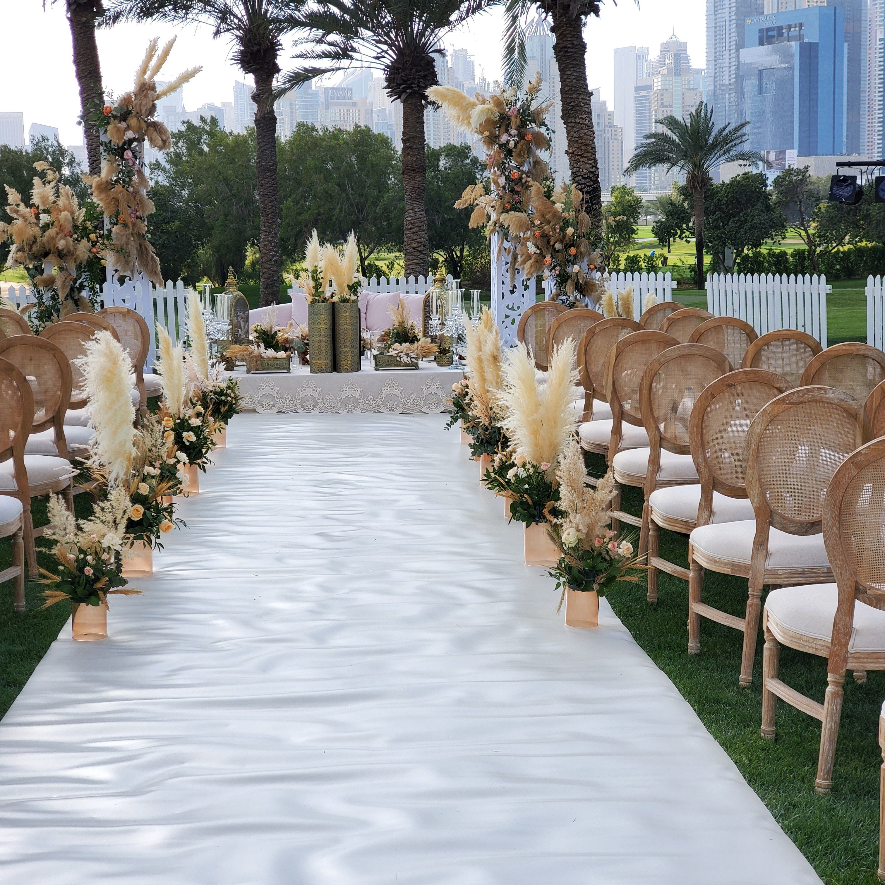 White aisle between rattan chairs and pampas grass urns leading to the ceremony table at Emirates Golf Club