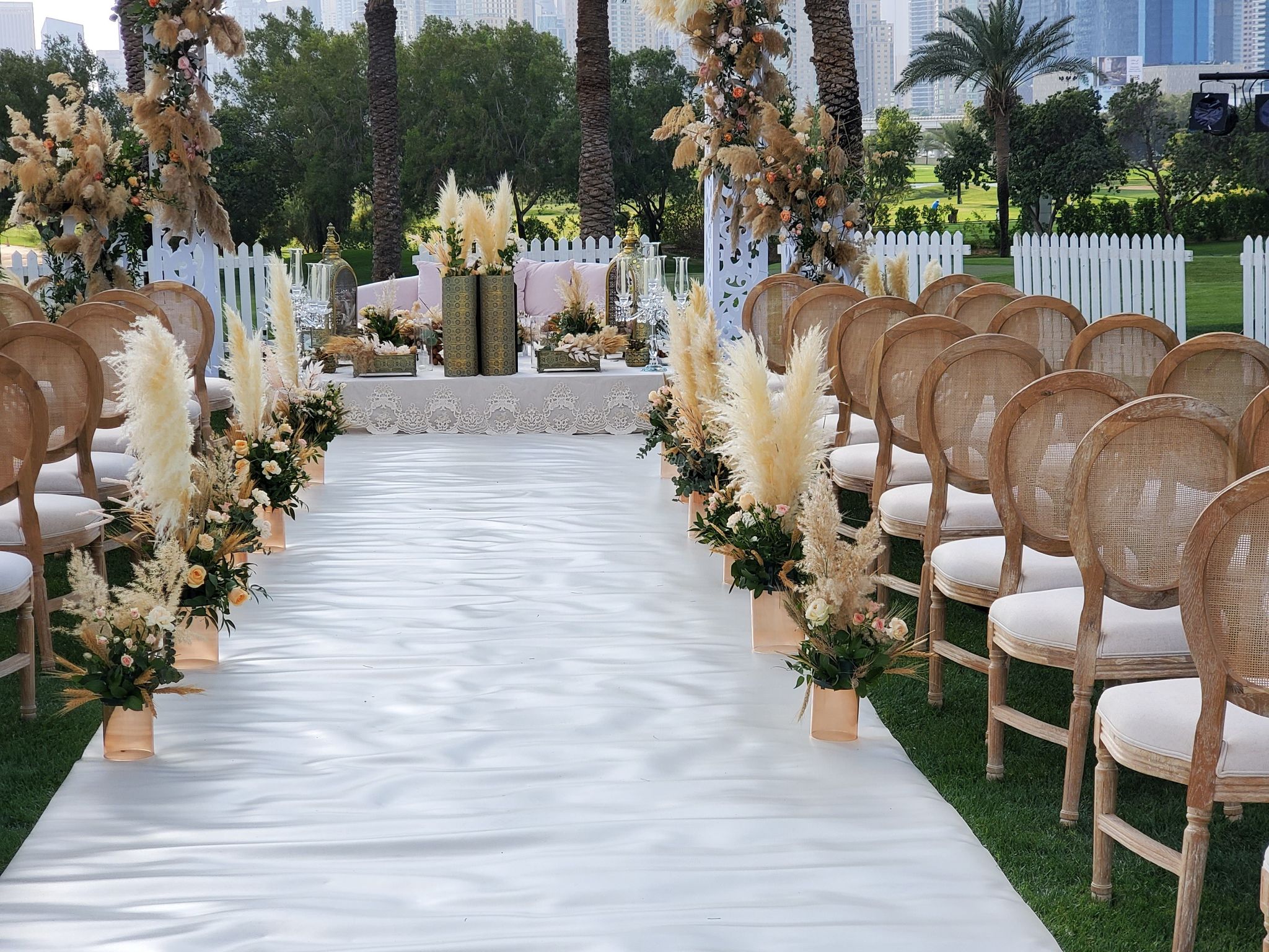 White aisle between rattan chairs and pampas grass urns leading to the ceremony table at Emirates Golf Club