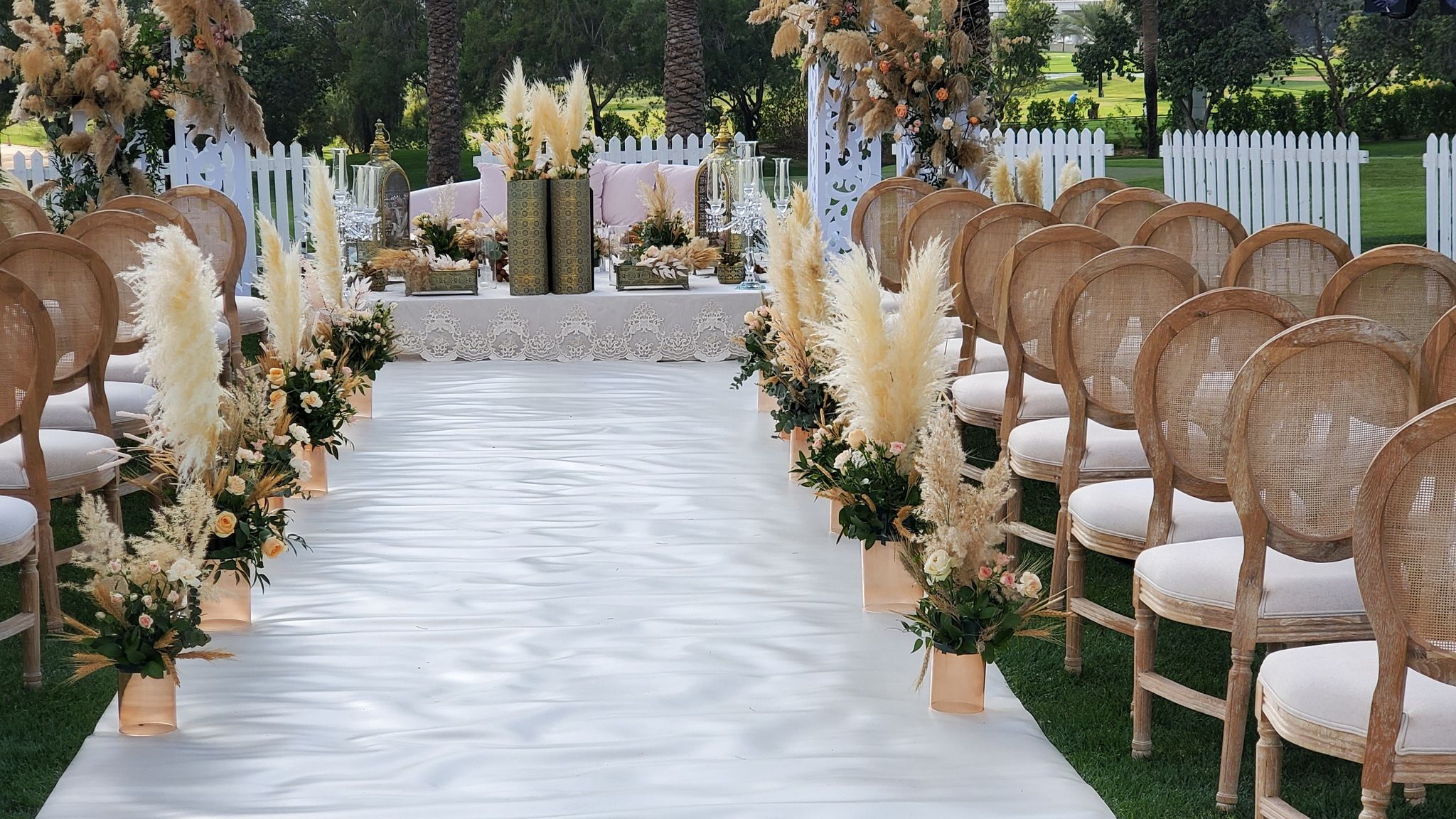 White aisle between rattan chairs and pampas grass urns leading to the ceremony table at Emirates Golf Club